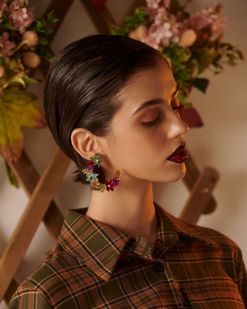 Person wearing colourful floral wreath earrings with a floral background