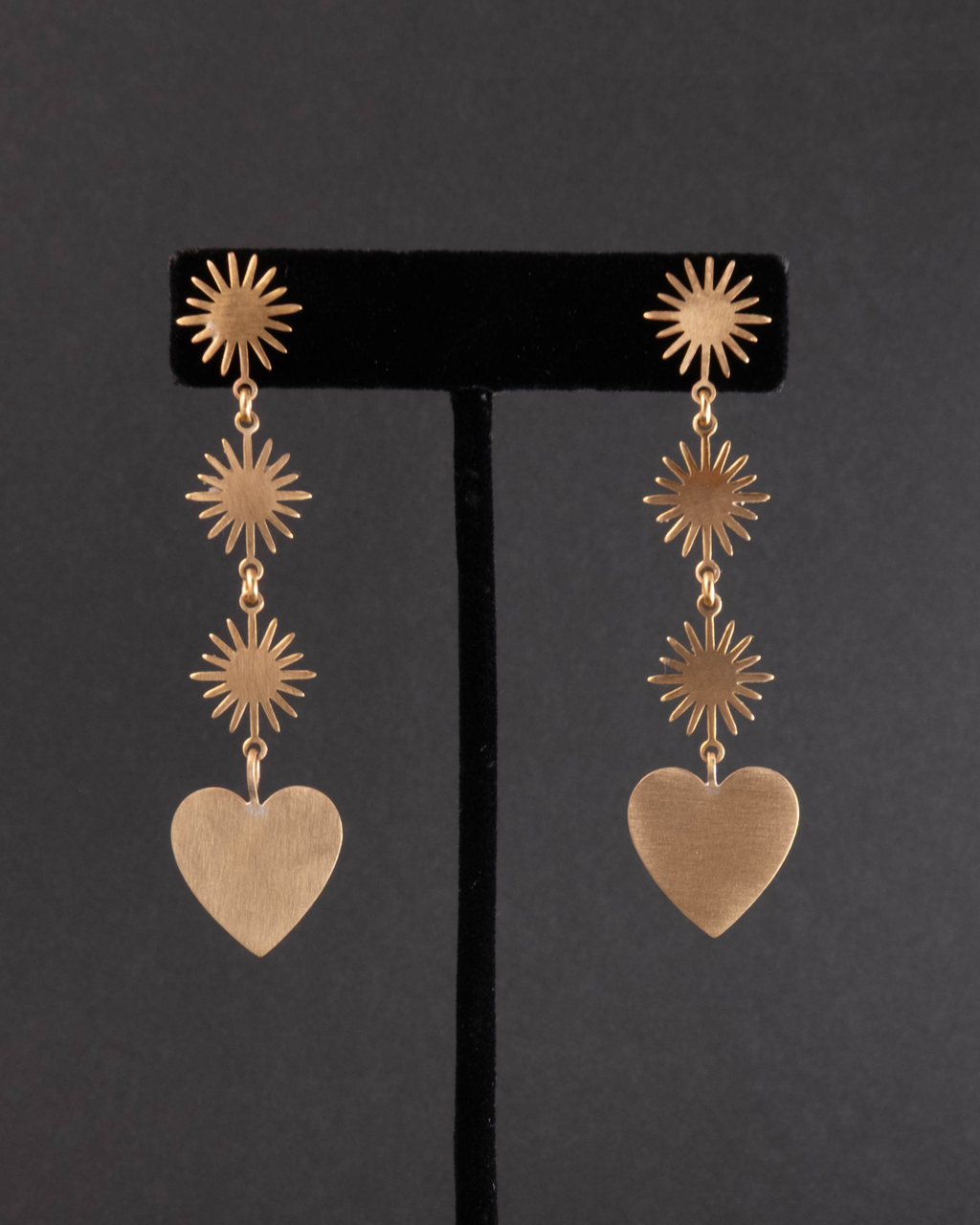 Gold heart-shaped earrings with star designs on a black stand against a dark background