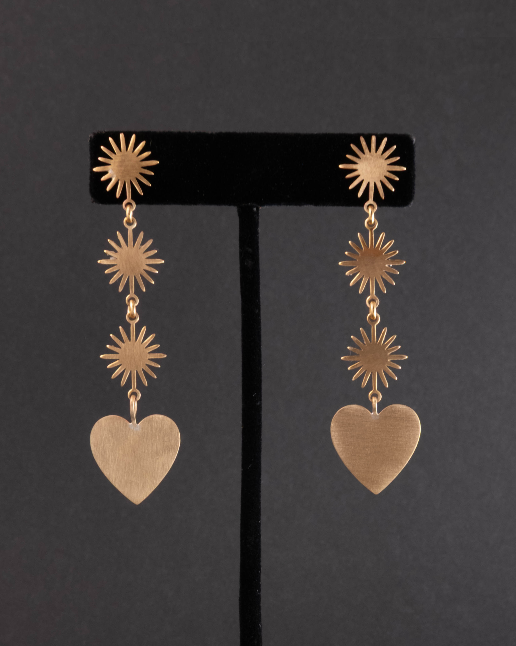 Gold heart-shaped earrings with star designs on a black stand against a dark background