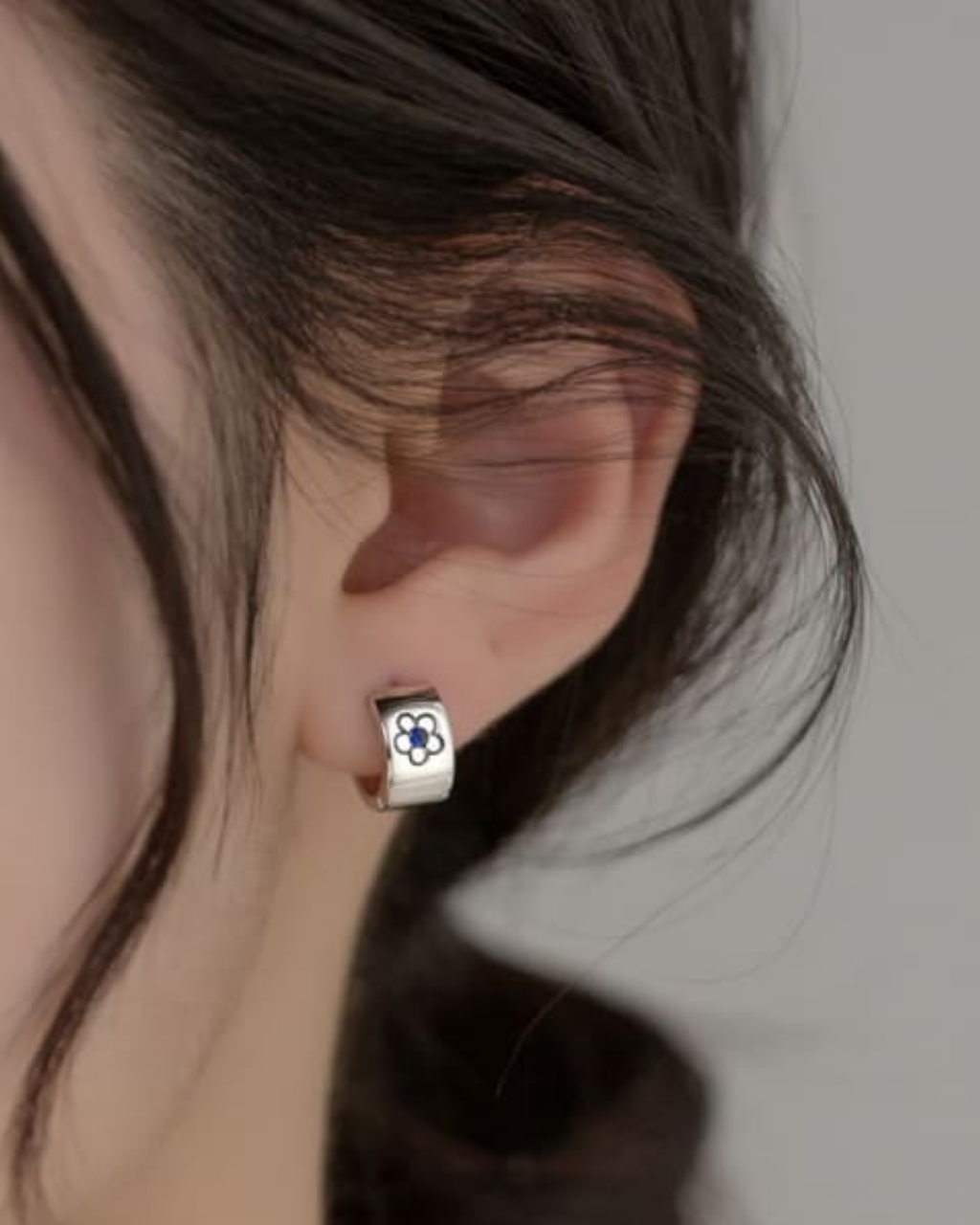 Silver hoop earring with a blue flower design worn by a person.