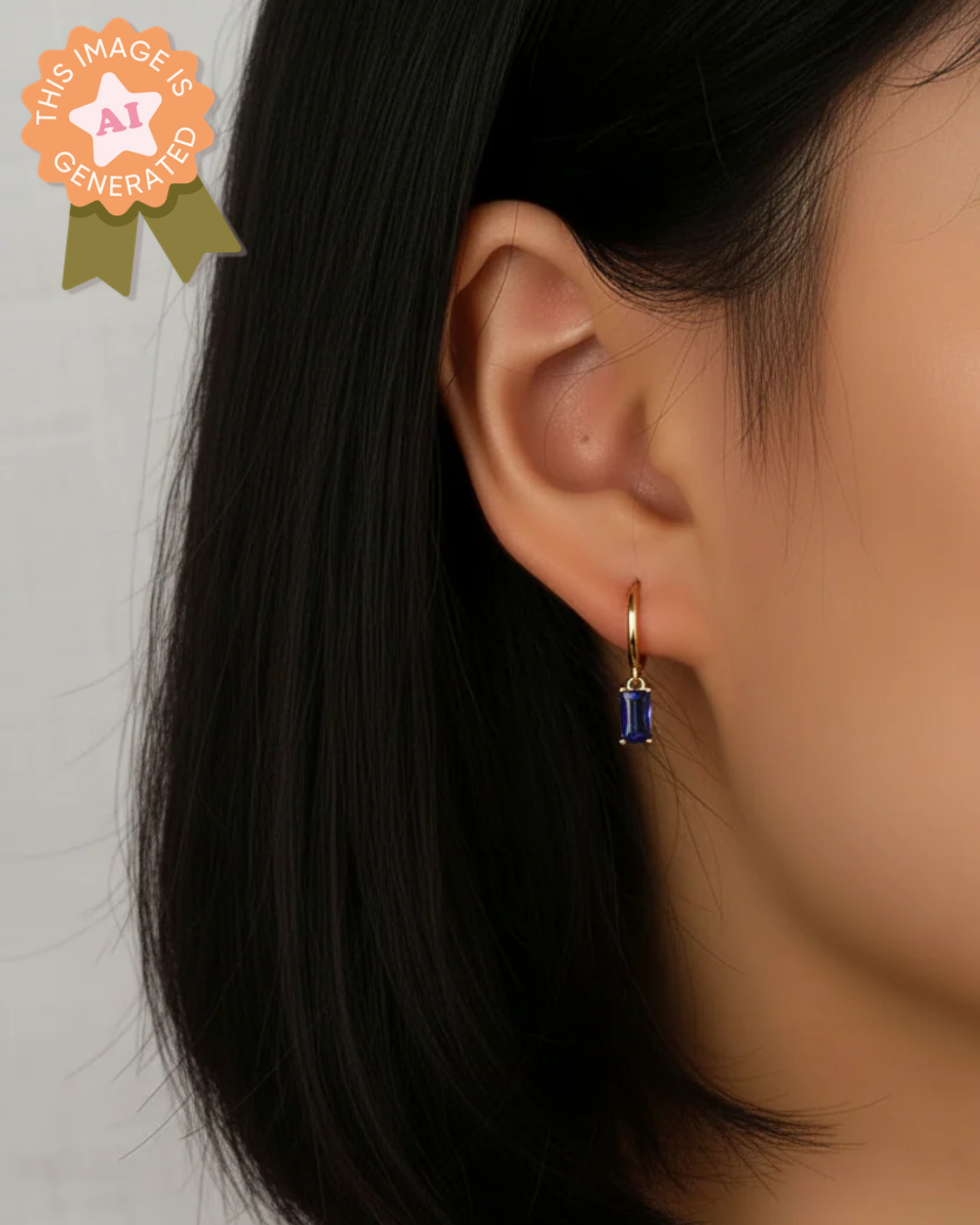 Close-up of an ear wearing a gold hoop earring with a blue gemstone on a plain background.