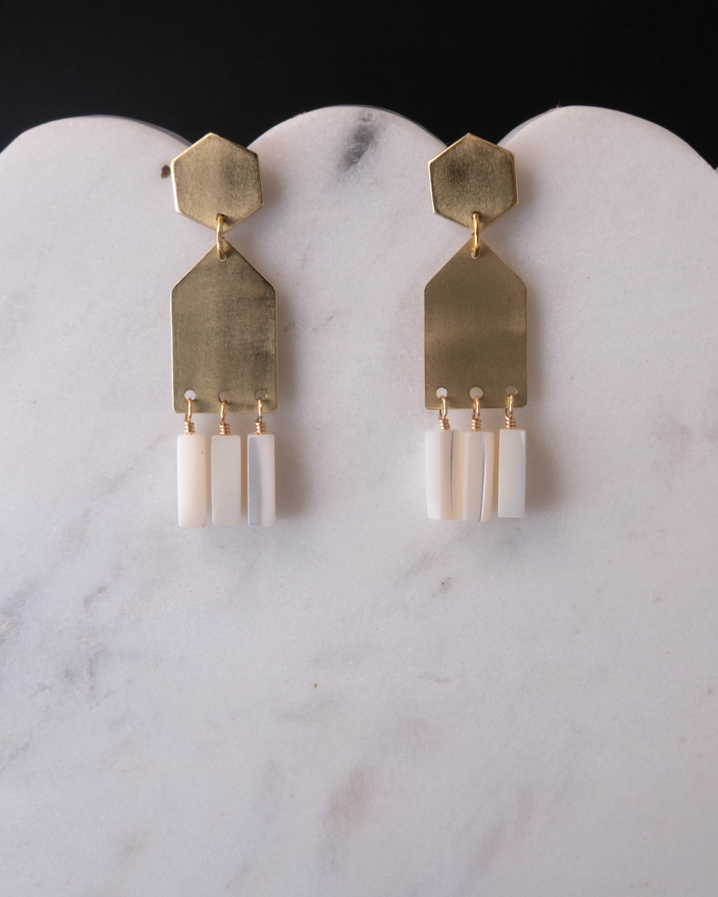 Gold and mother of pearl earrings on a marble surface