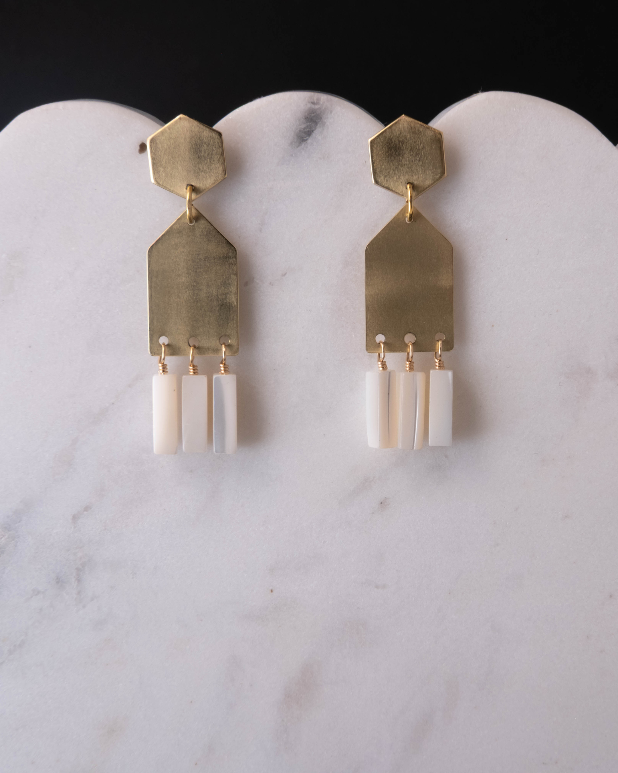 Gold and mother of pearl earrings on a marble surface