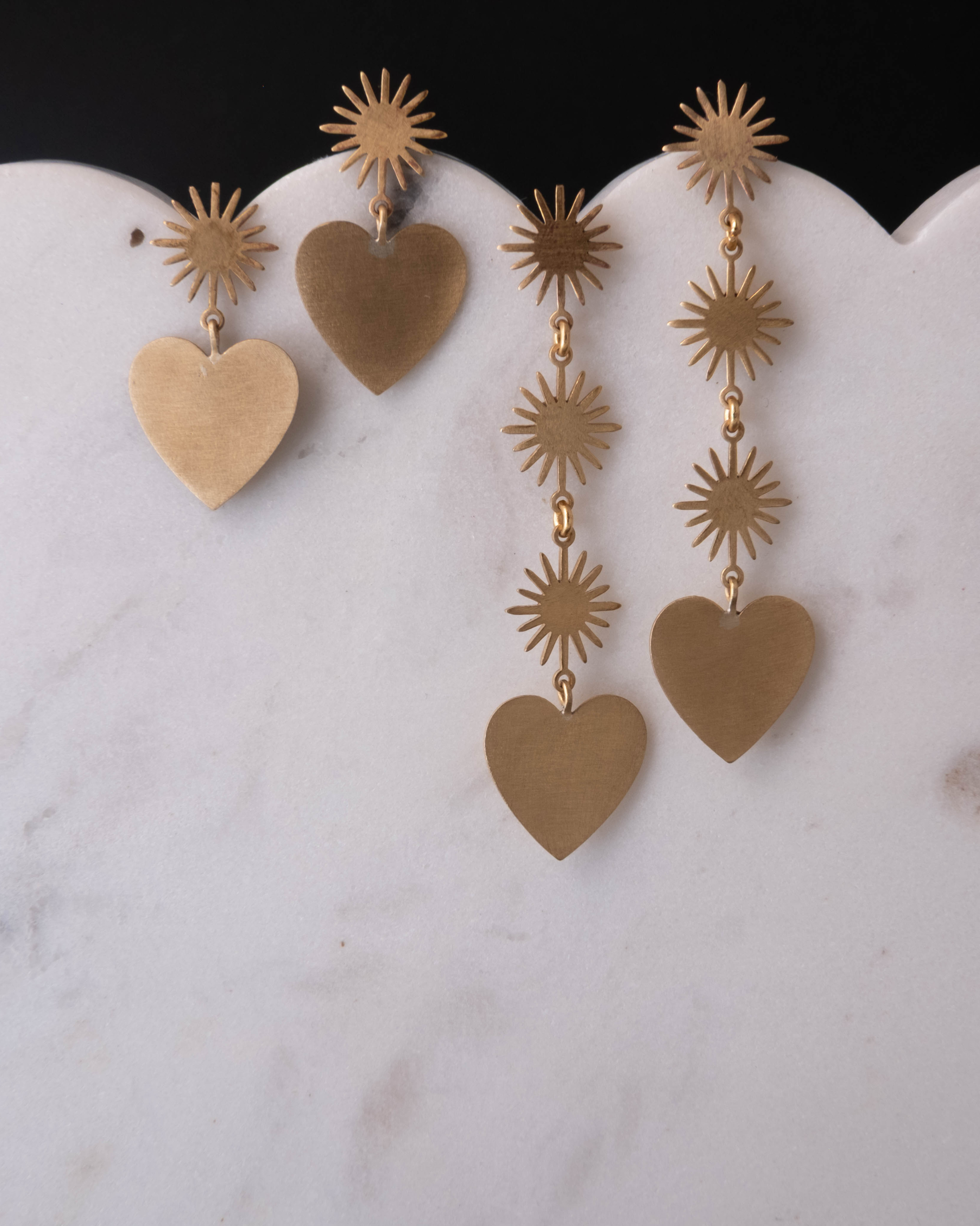 Gold heart-shaped earrings with starburst designs on a marble surface