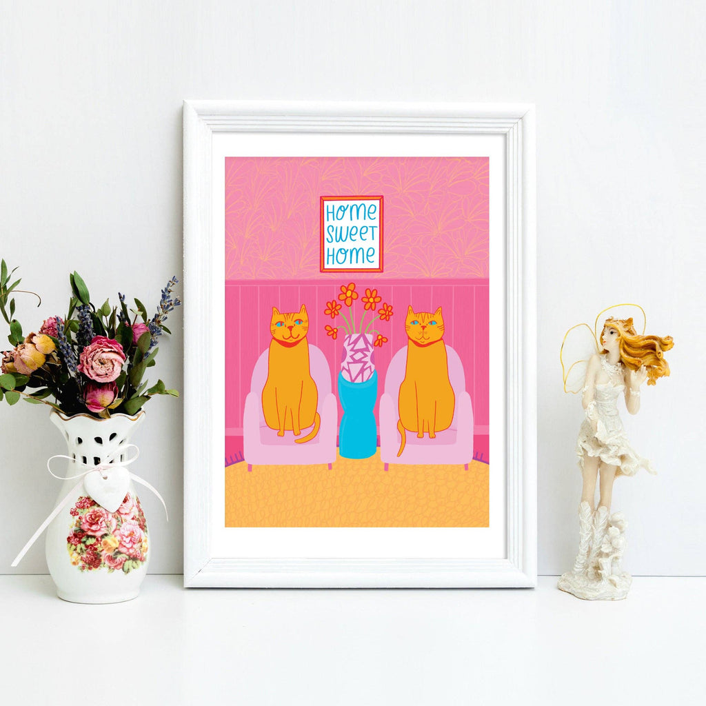 Framed artwork with two cats, a woman, and 'home sweet home' text on a pink background.