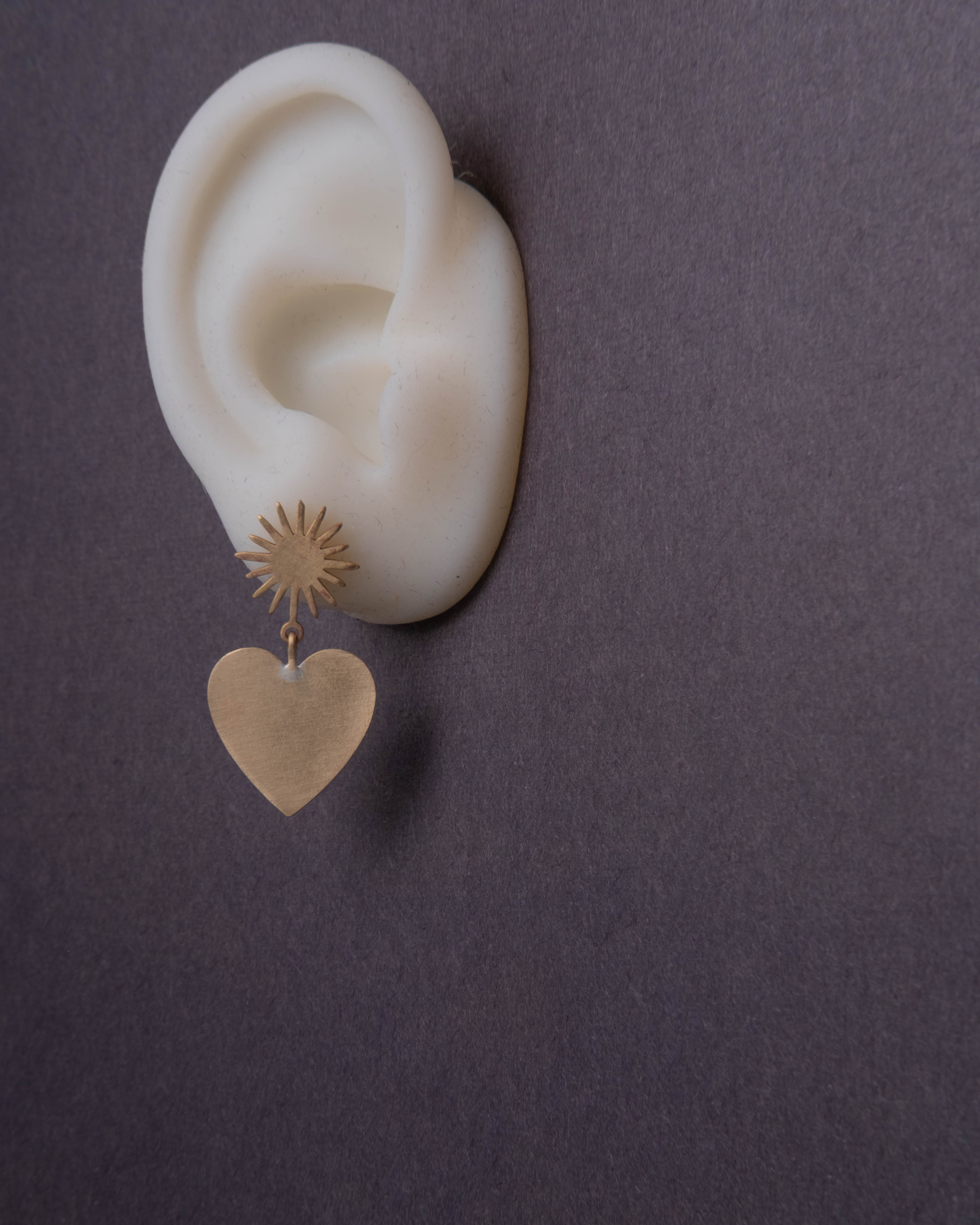 Gold heart-shaped earring on a white ear with a dark background
