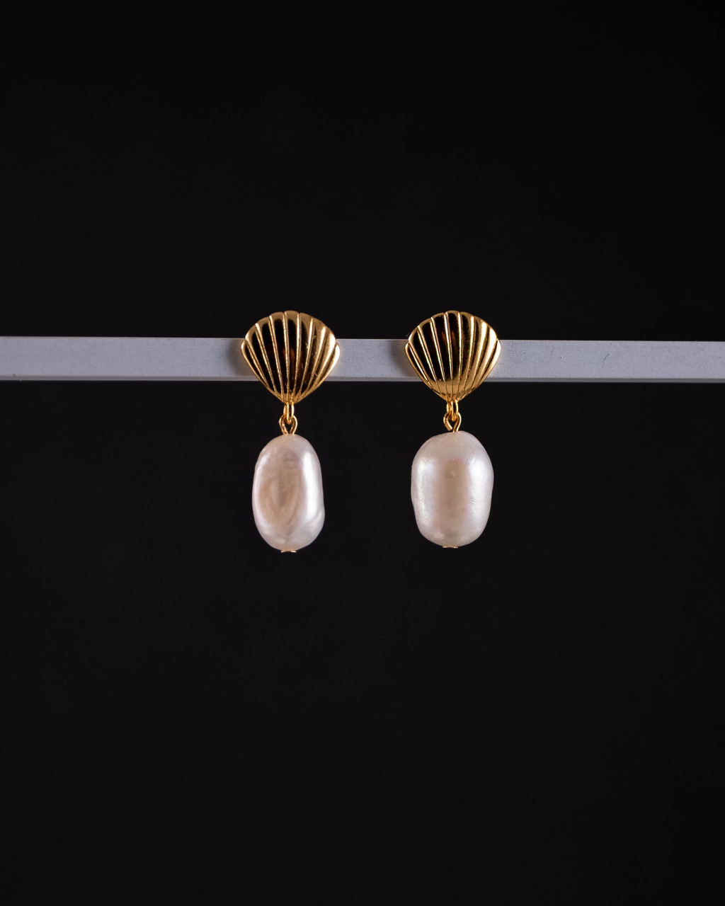 Gold shell earrings with pearl drops on a black background