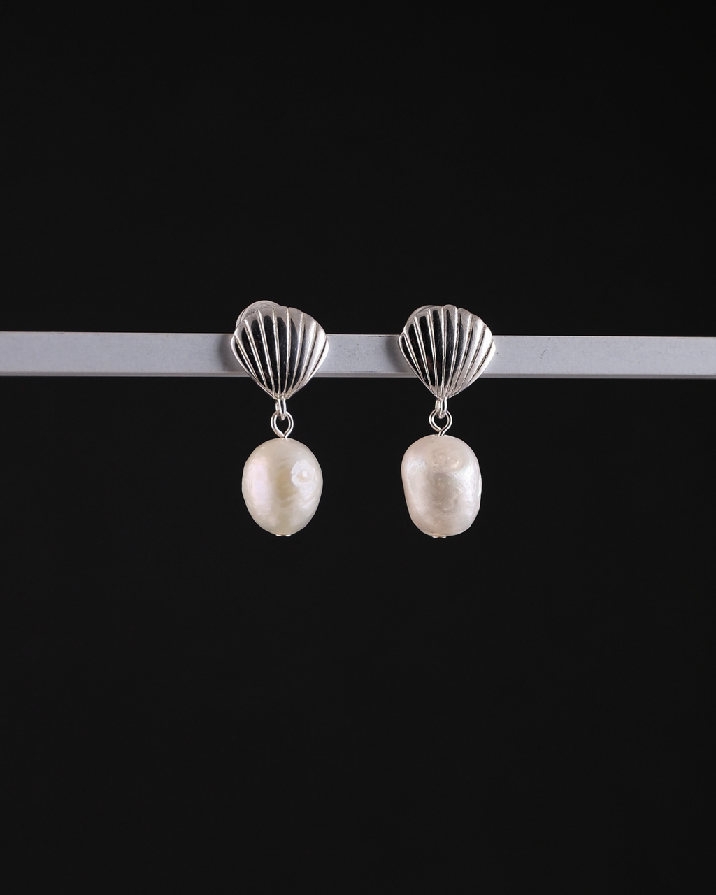 Pair of earrings with sterling silver shell tops and pearls on a black background