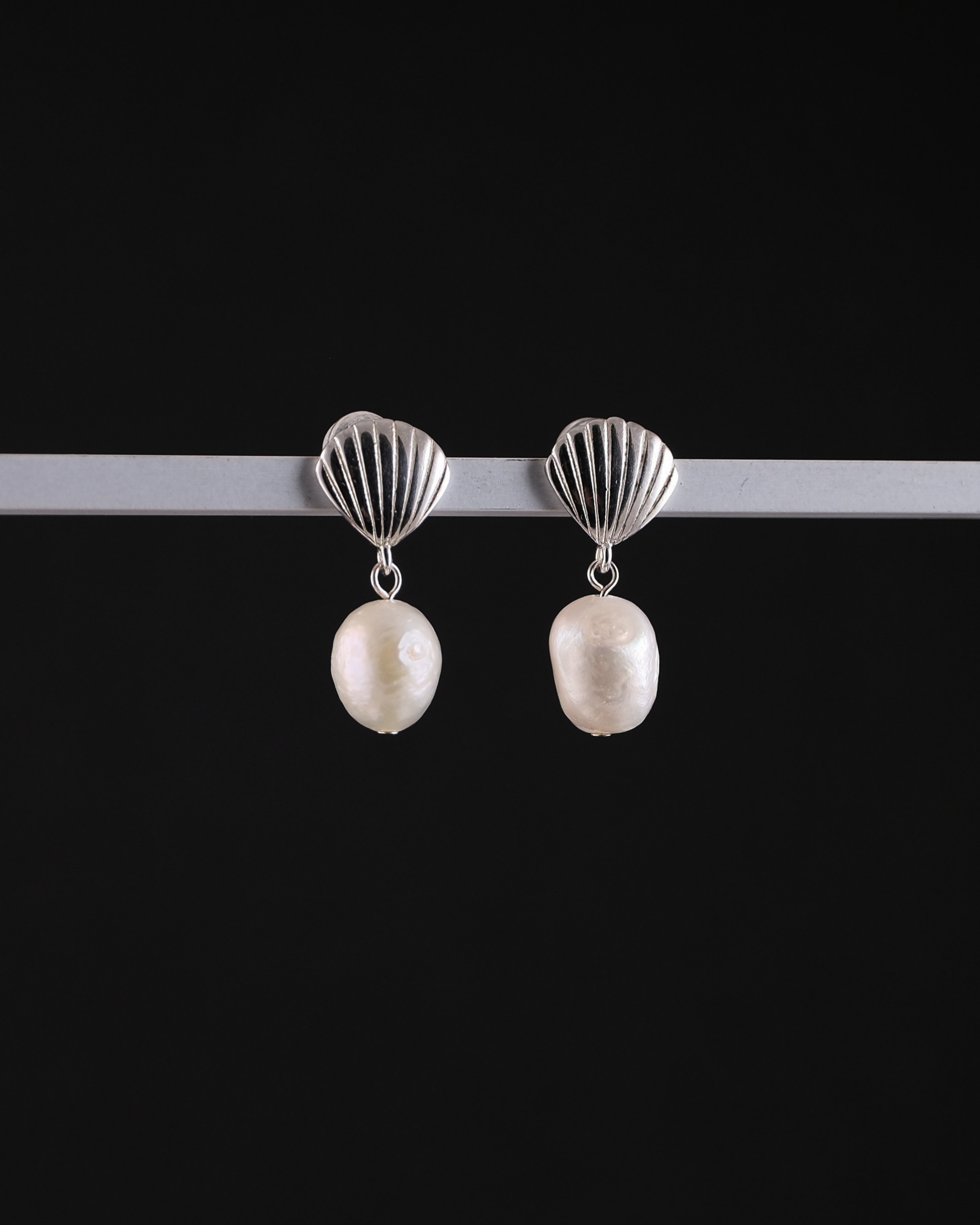 Pair of earrings with sterling silver shell tops and pearls on a black background
