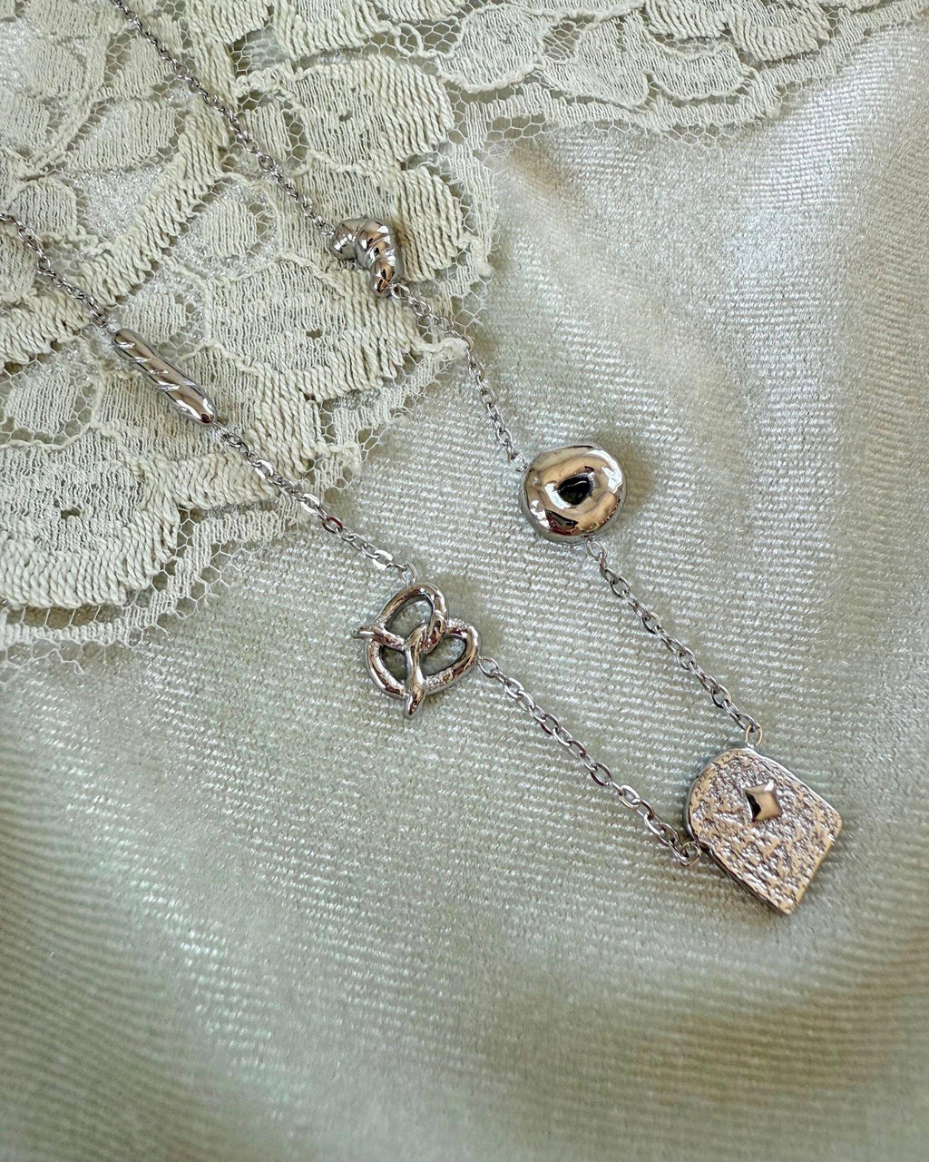 Silver necklace with bread-shaped pendants on a textured fabric background