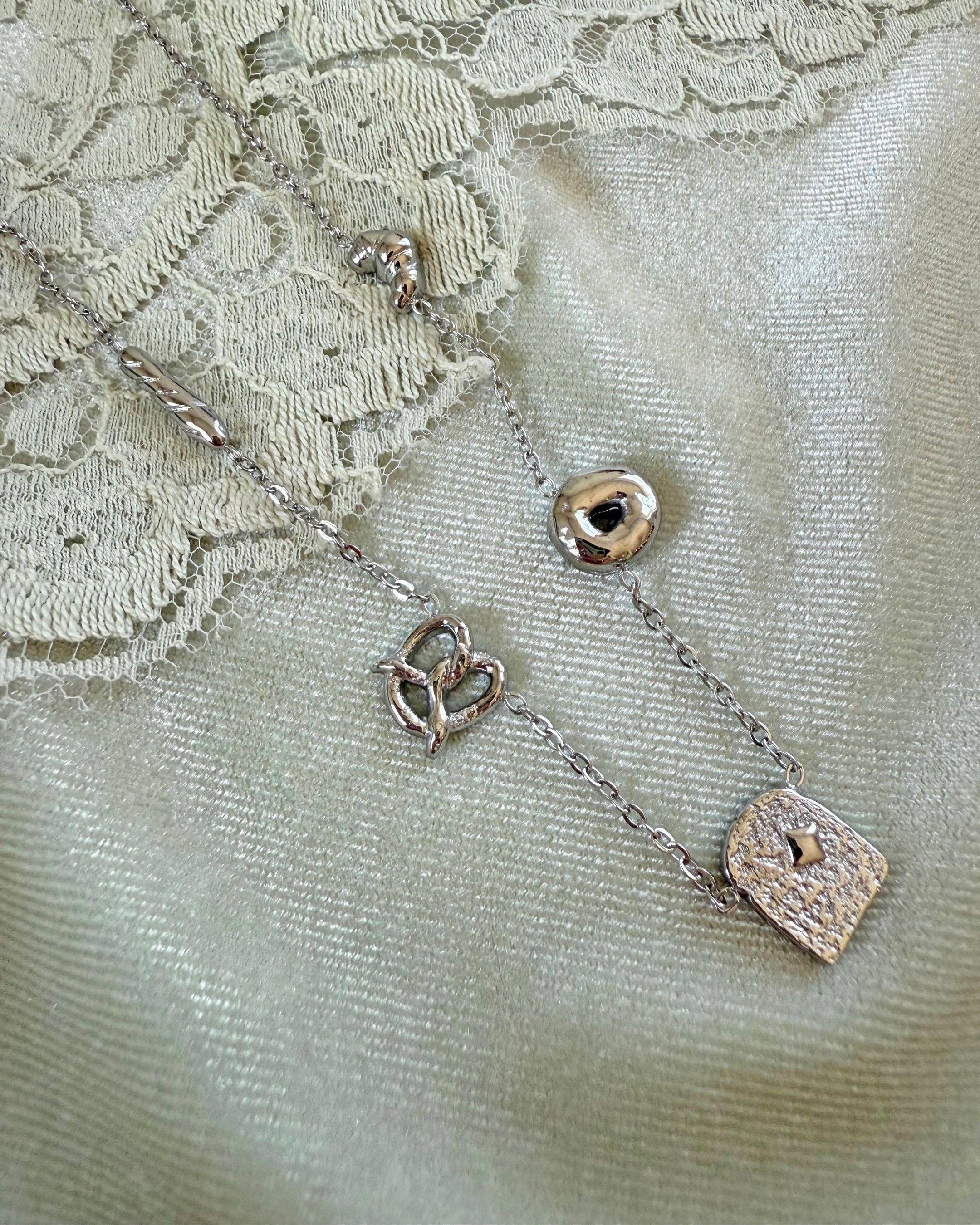Silver necklace with bread-shaped pendants on a textured fabric background