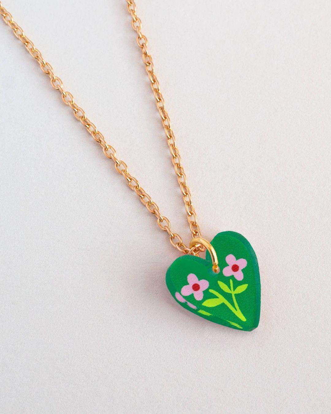 Green heart-shaped pendant with floral design on a gold chain against a light gray background