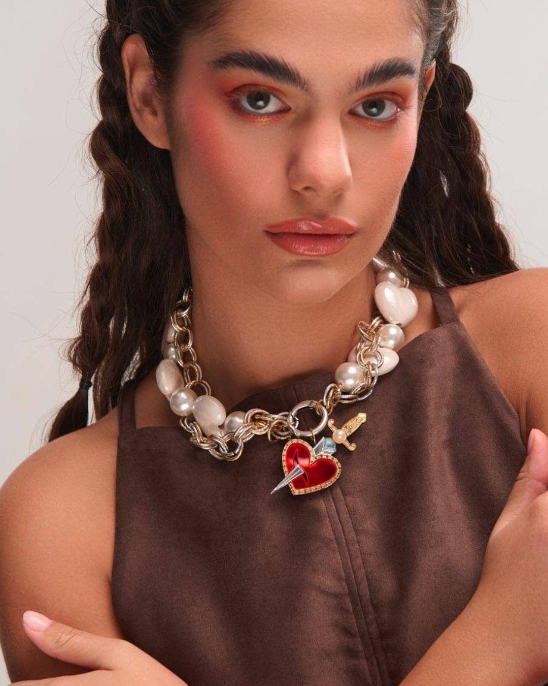 Person wearing a necklace with heart and sword charms against a plain background