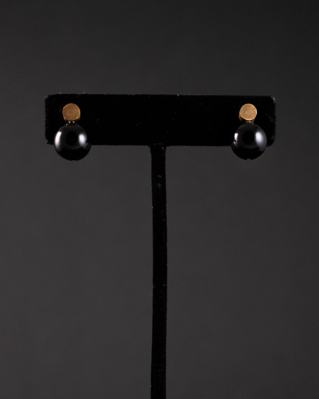 Black earrings on a black stand against a dark background