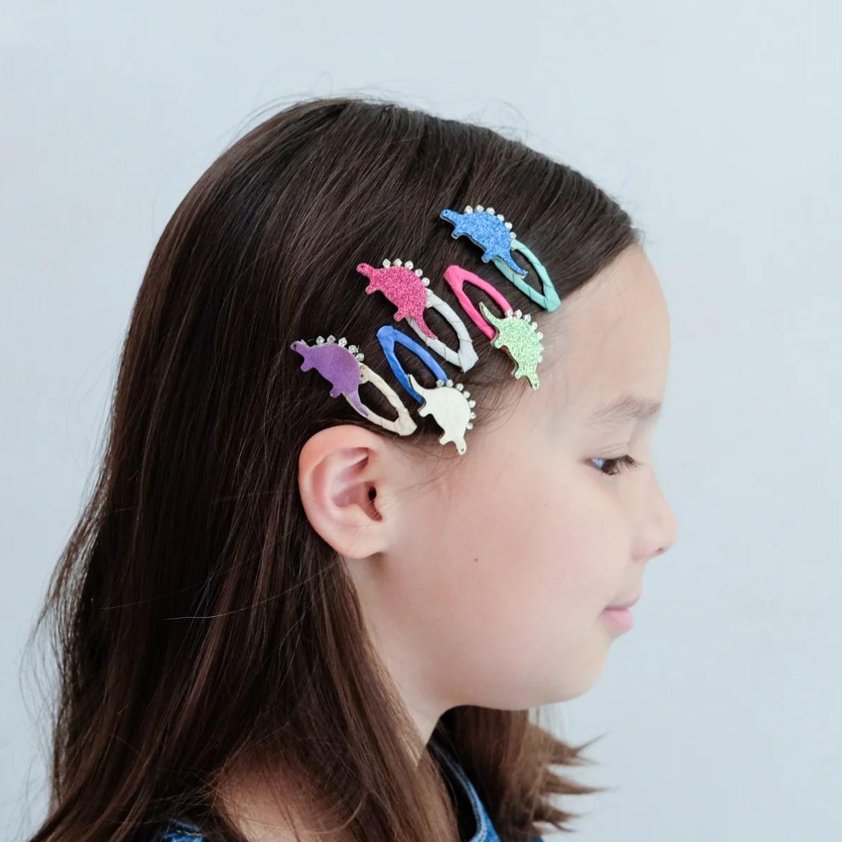 Girl with colorful dinosaur hair clips in her hair against a light gray background
