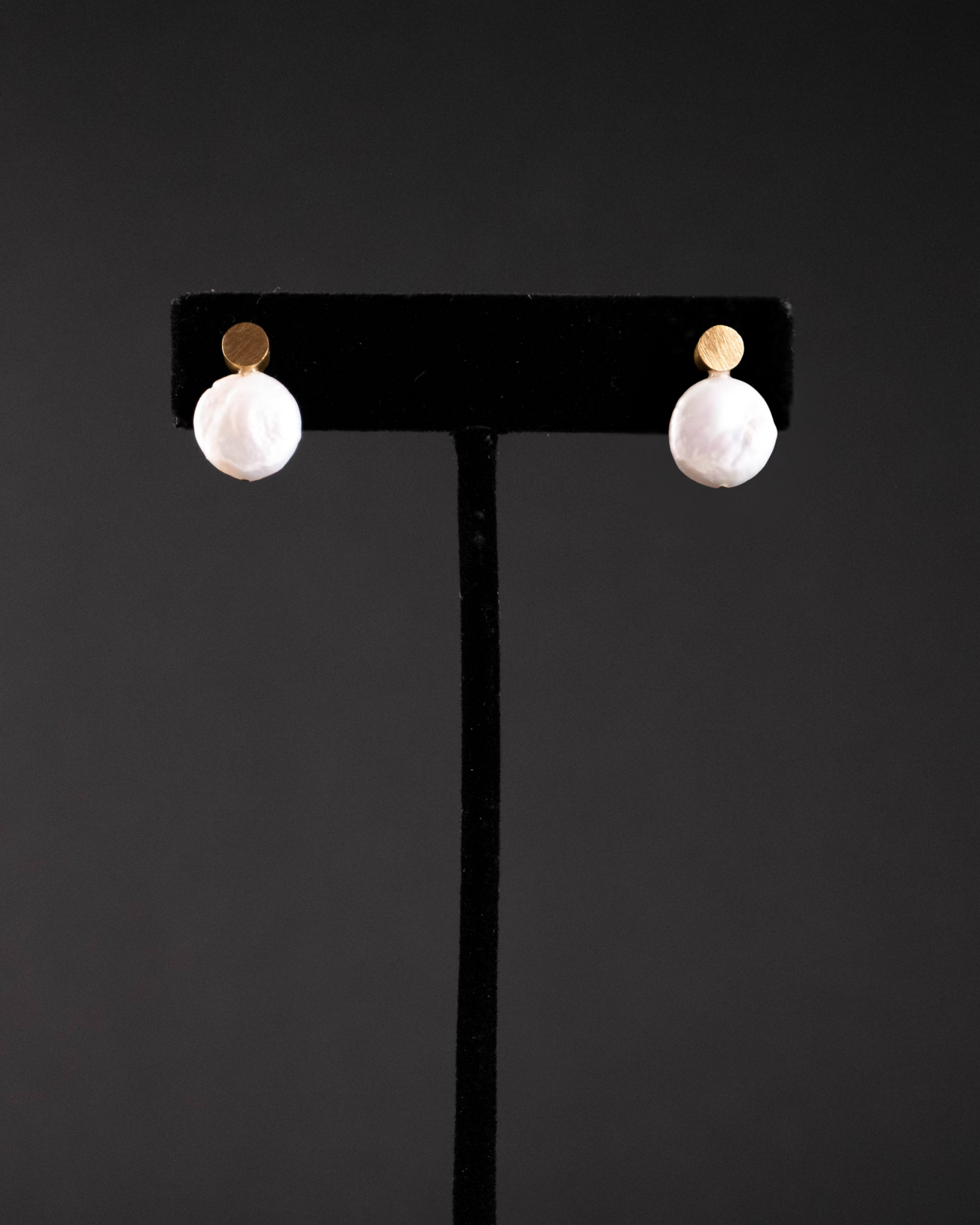Pair of pearl earrings on a black earring stand against a dark background