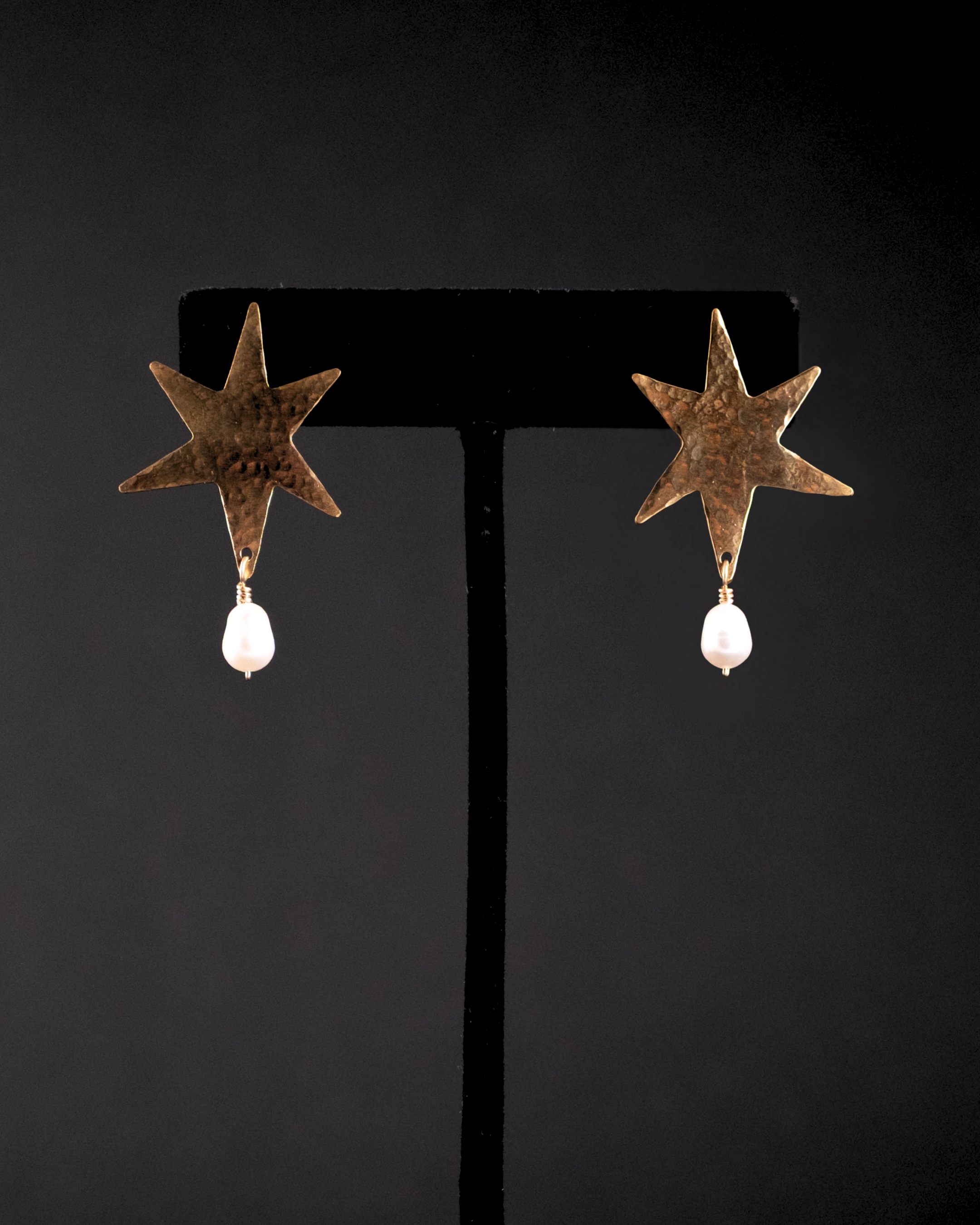 Star-shaped earrings with pearl drops on a black stand against a black background