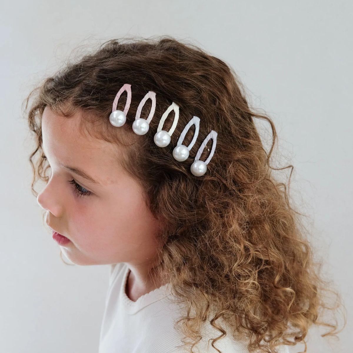 Child wearing a decorative hair accessory with pearls and white beads on a plain background