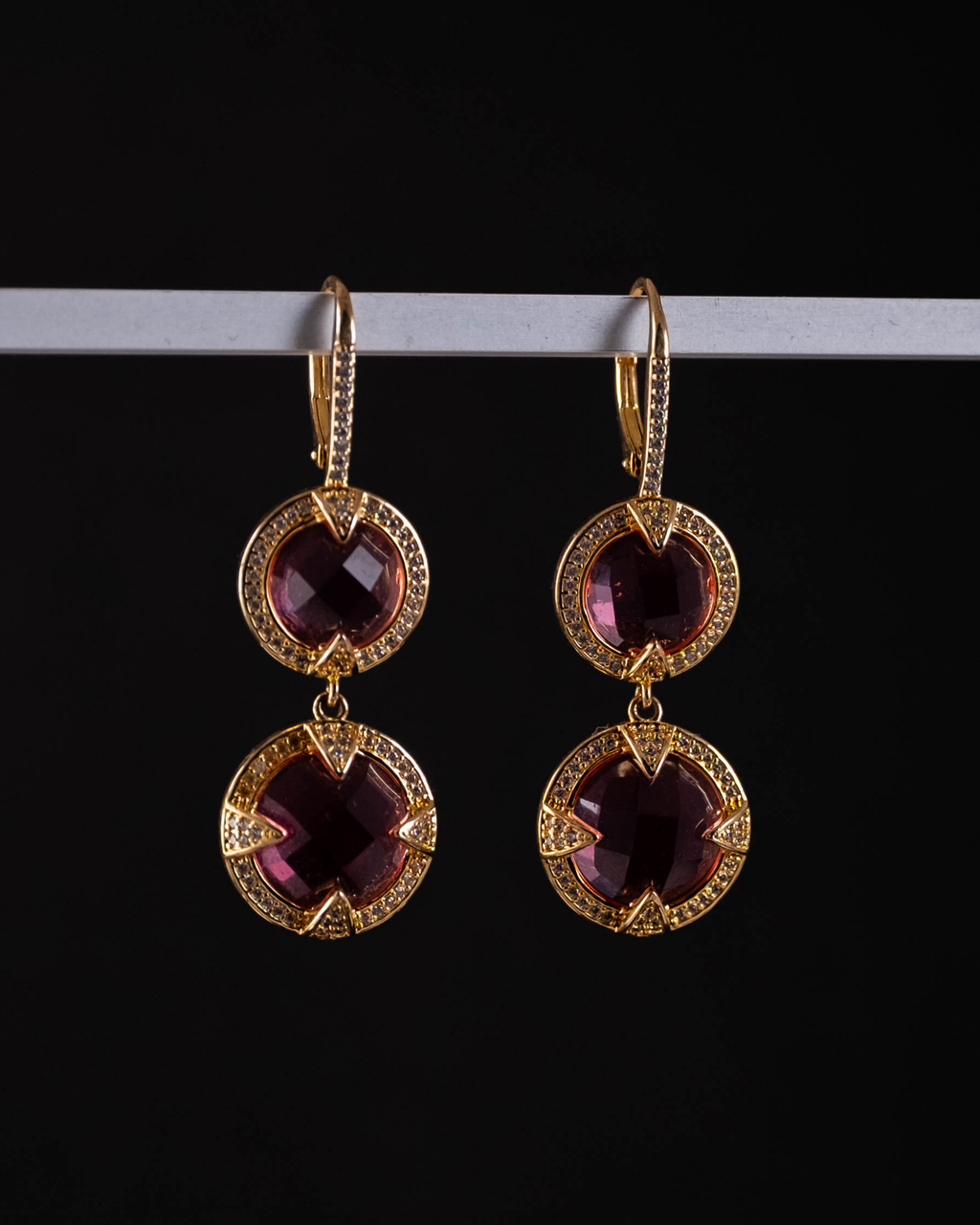 Gold earrings with pink gemstones on a black background