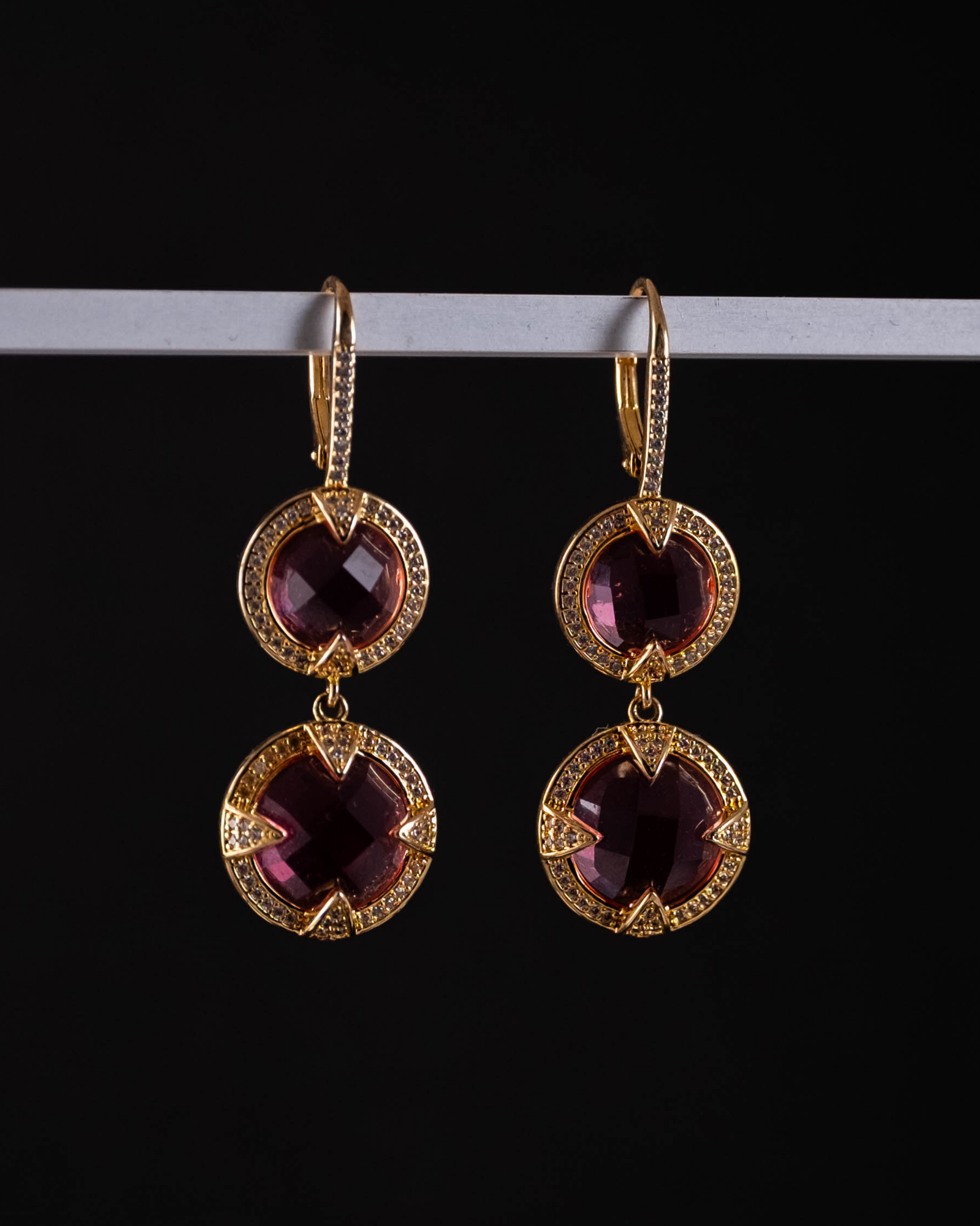 Gold earrings with pink gemstones on a black background