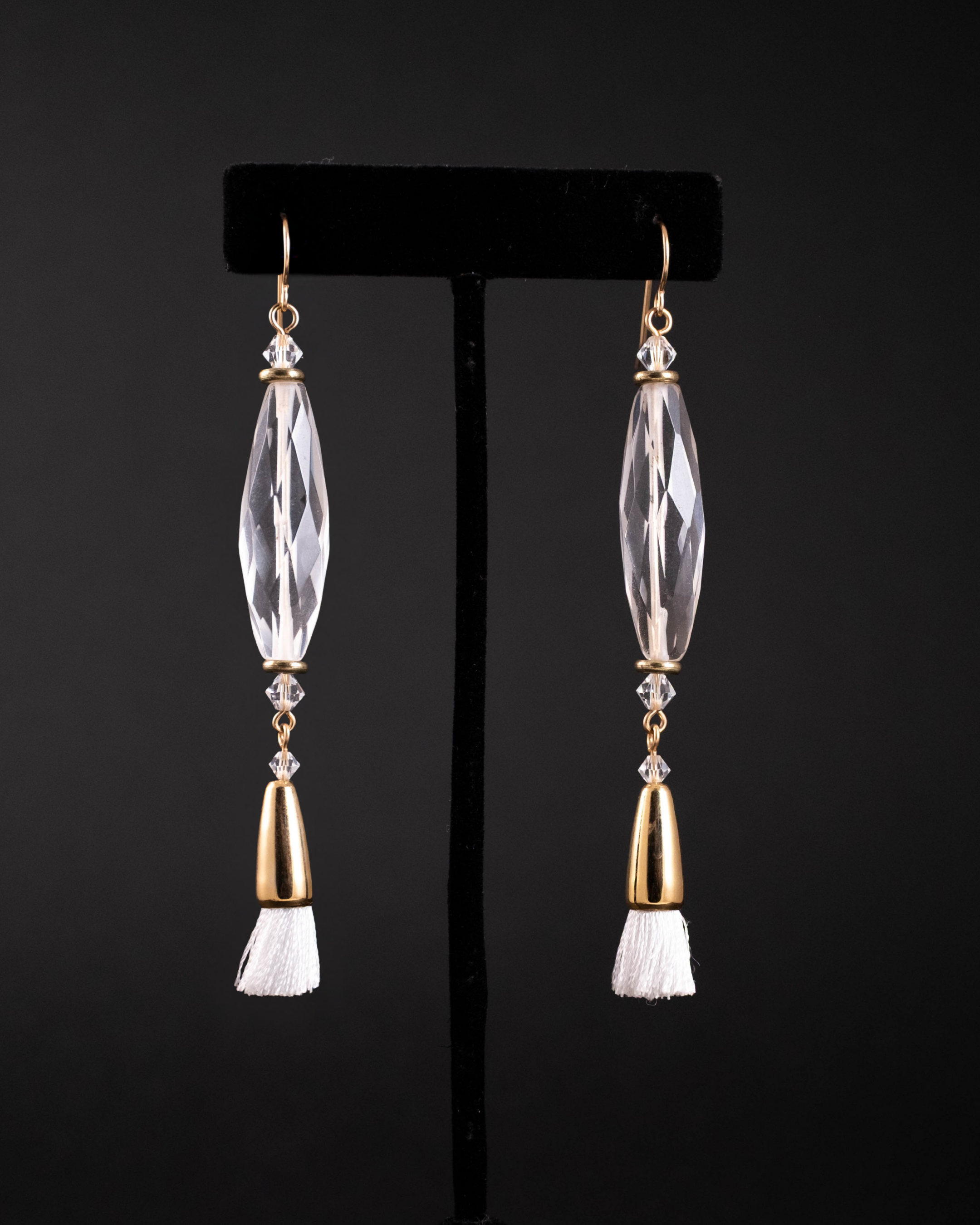 Pair of earrings with clear quartz and gold accents on a black stand.