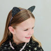 Child wearing a black glittery cat ear headband on a plain background