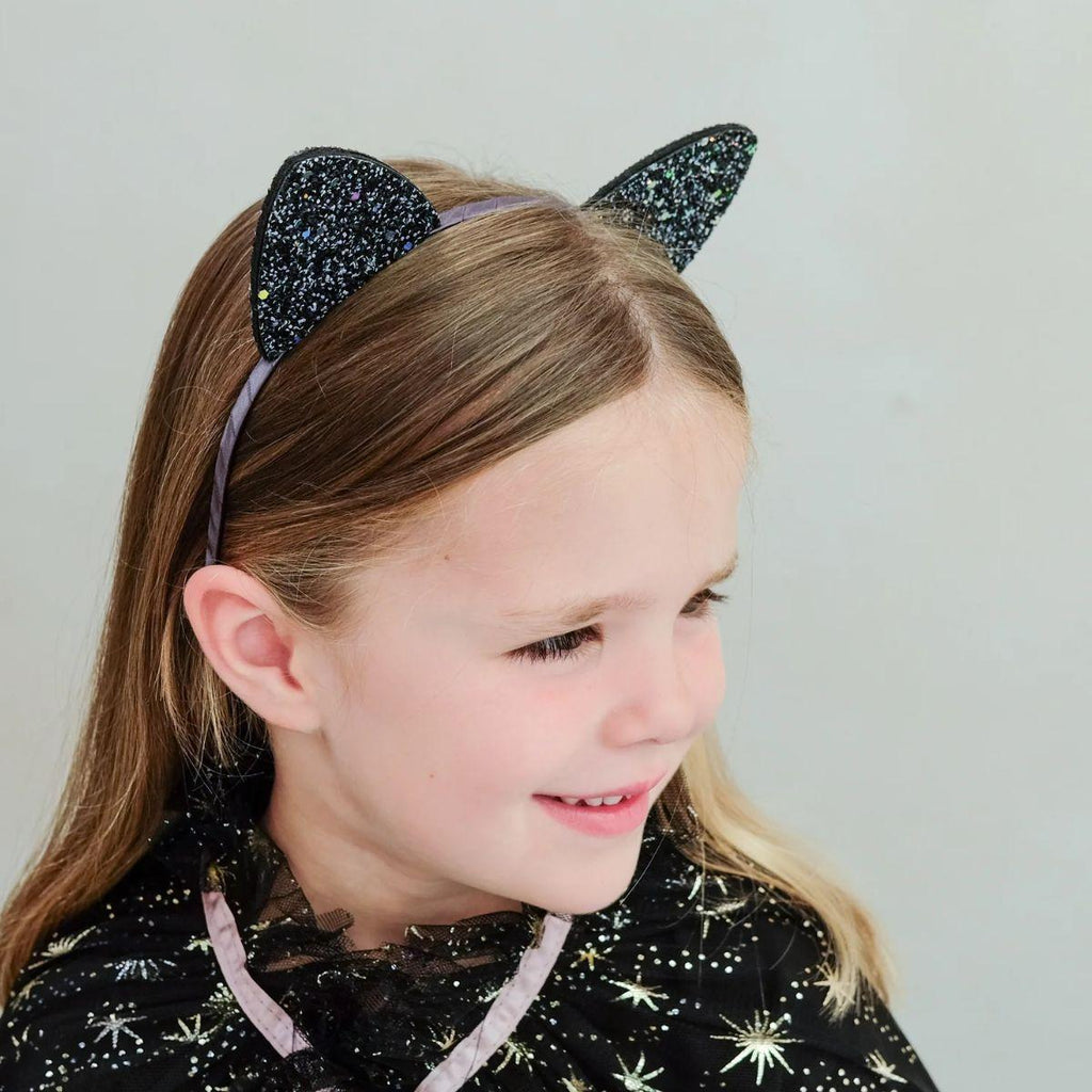 Child wearing a black glittery cat ear headband on a plain background