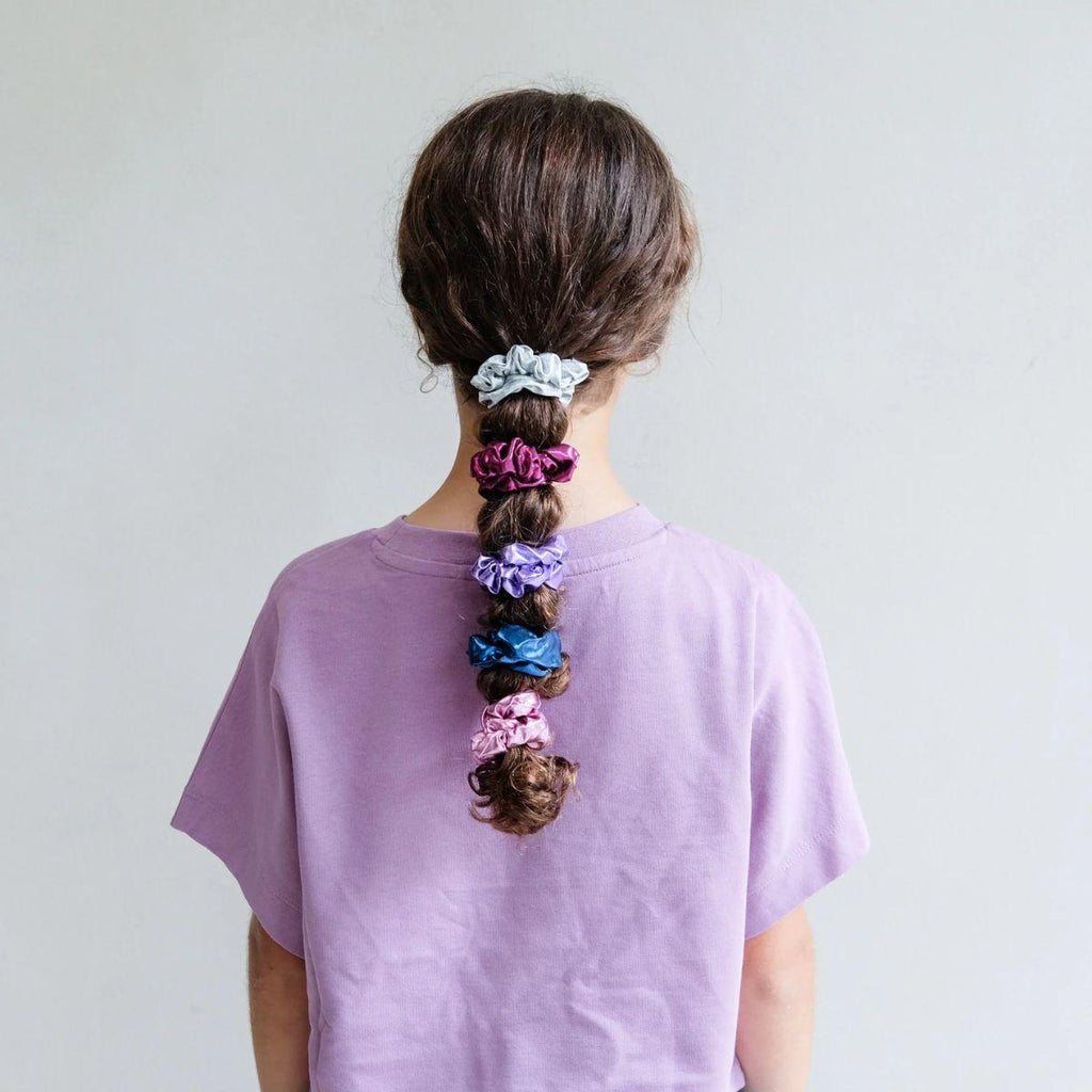 Person with a long braid holding colorful scrunchies against a plain background