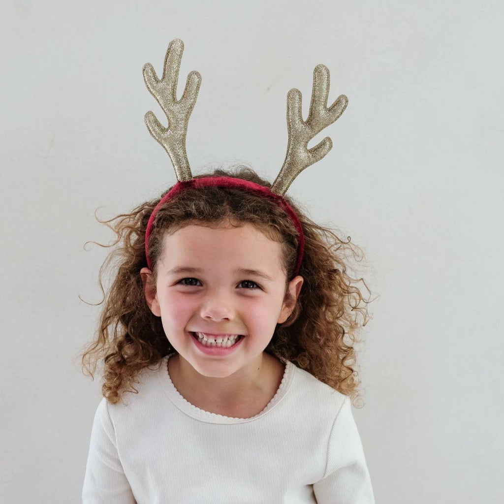 Child wearing a headband with gold glittery antlers against a plain background