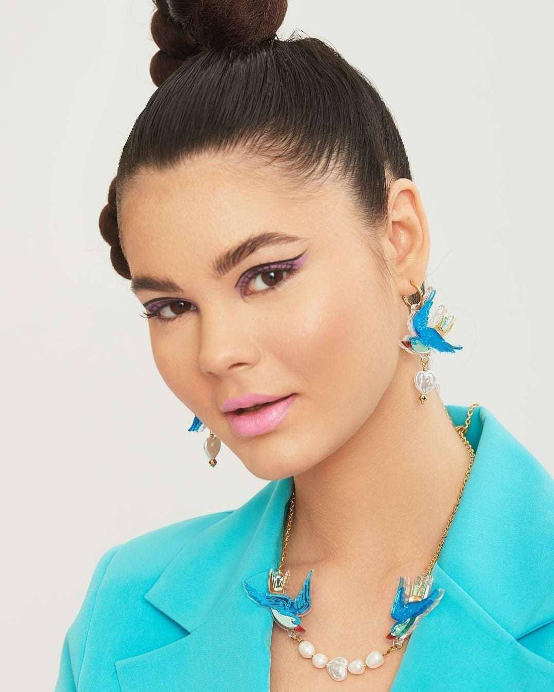 Person wearing a turquoise outfit with swallow earrings against a light background