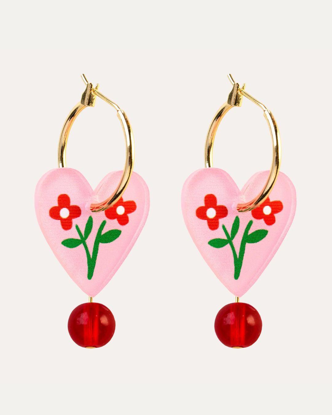 Heart-shaped earrings with floral design and red beads on a white background
