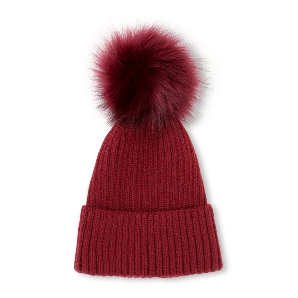 flatlay of a winter knitted beanie with faux fur pompom in red