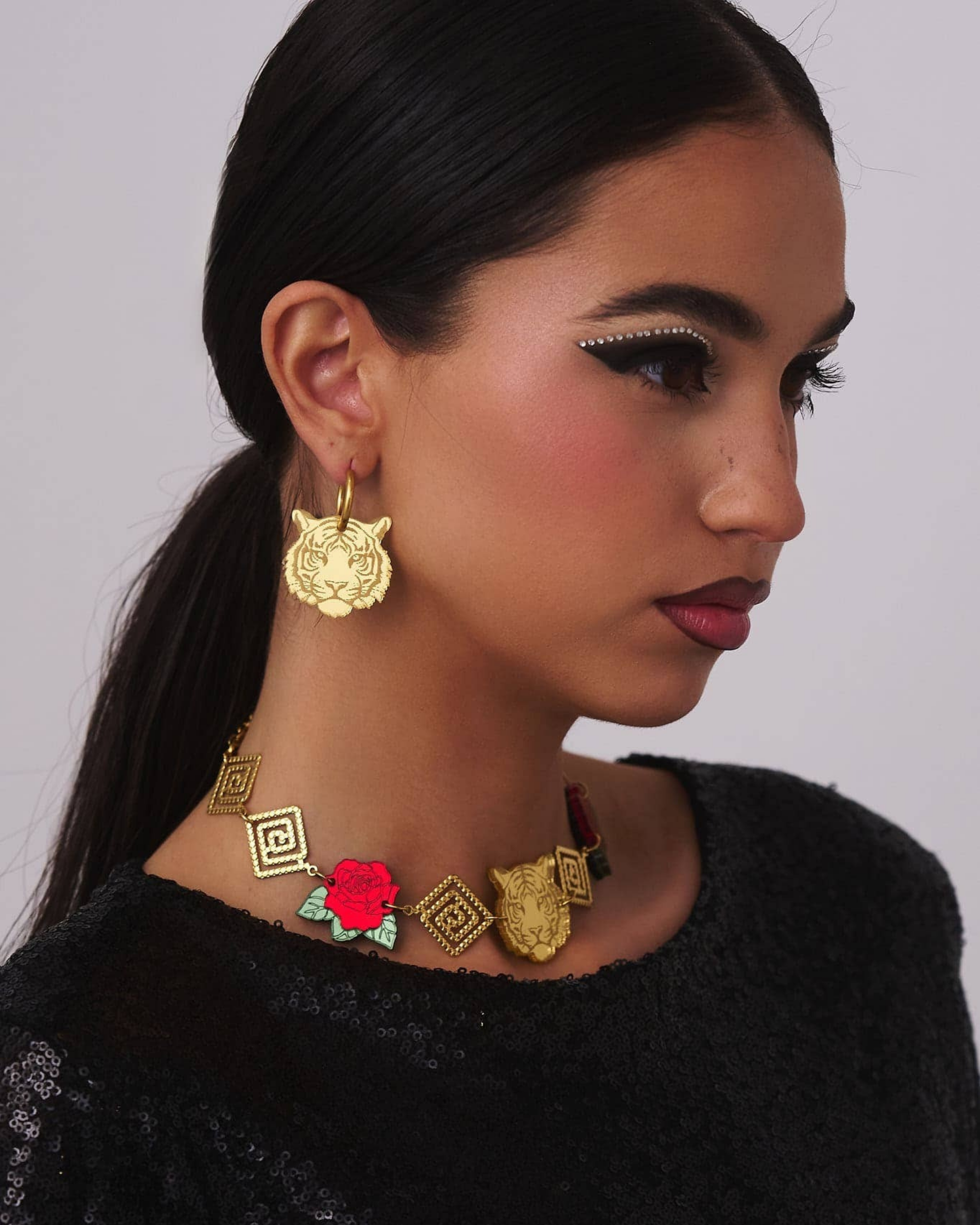 Person wearing gold tiger earrings with intricate designs on a plain background