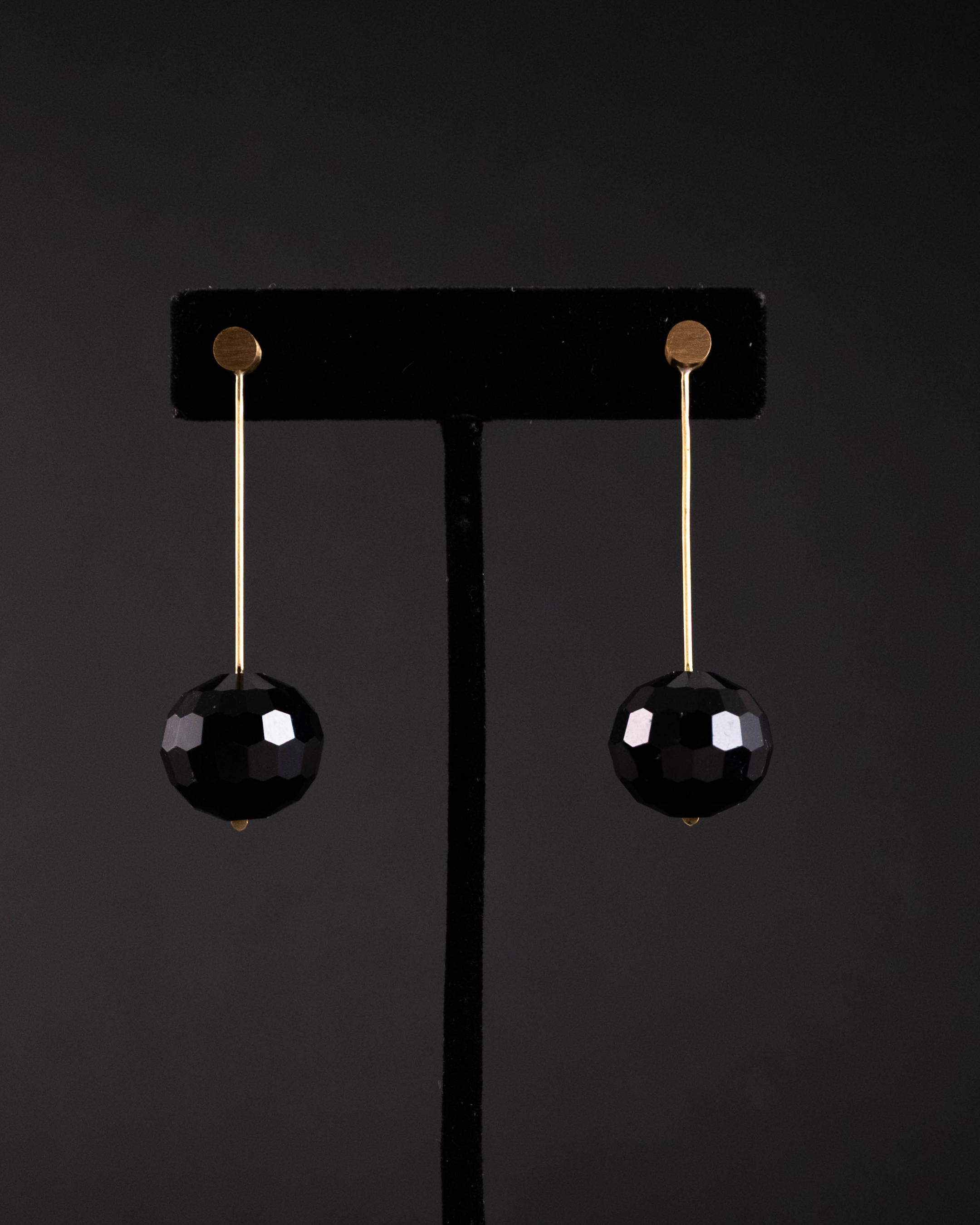 Black faceted earrings on a black stand against a black background