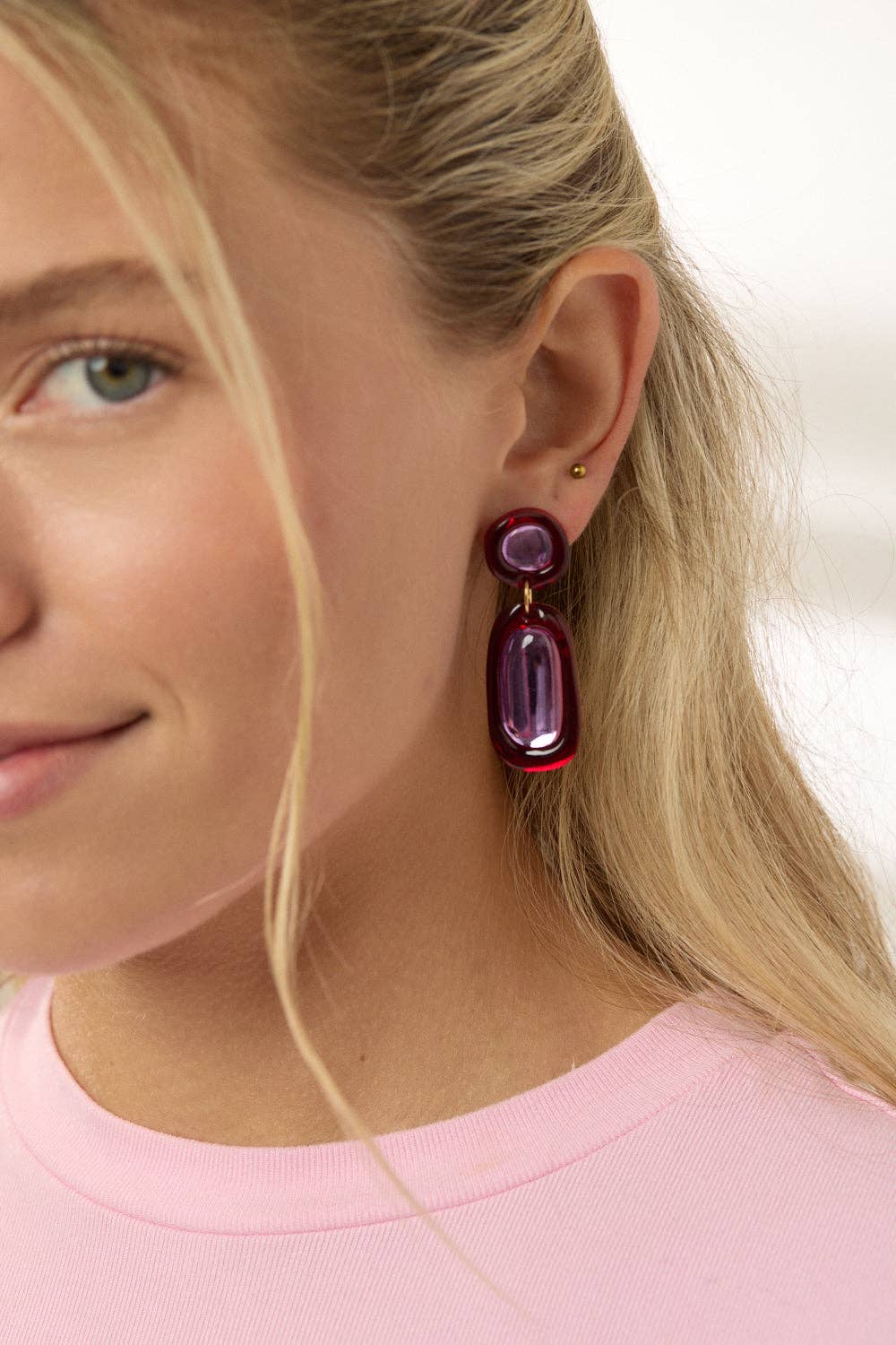 Close-up of a female presenting person wearing a purple and red earring with a blurred background