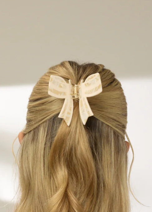 Person with styled long hair featuring a yellow bow, wearing a dark blue dress, against a neutral background.