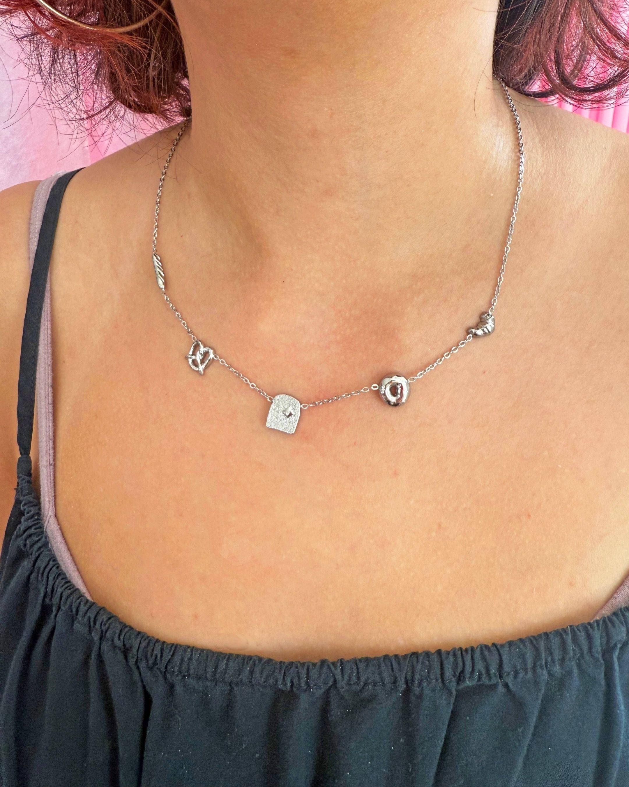 Silver necklace with small pendants on a person wearing a black top against a pink background