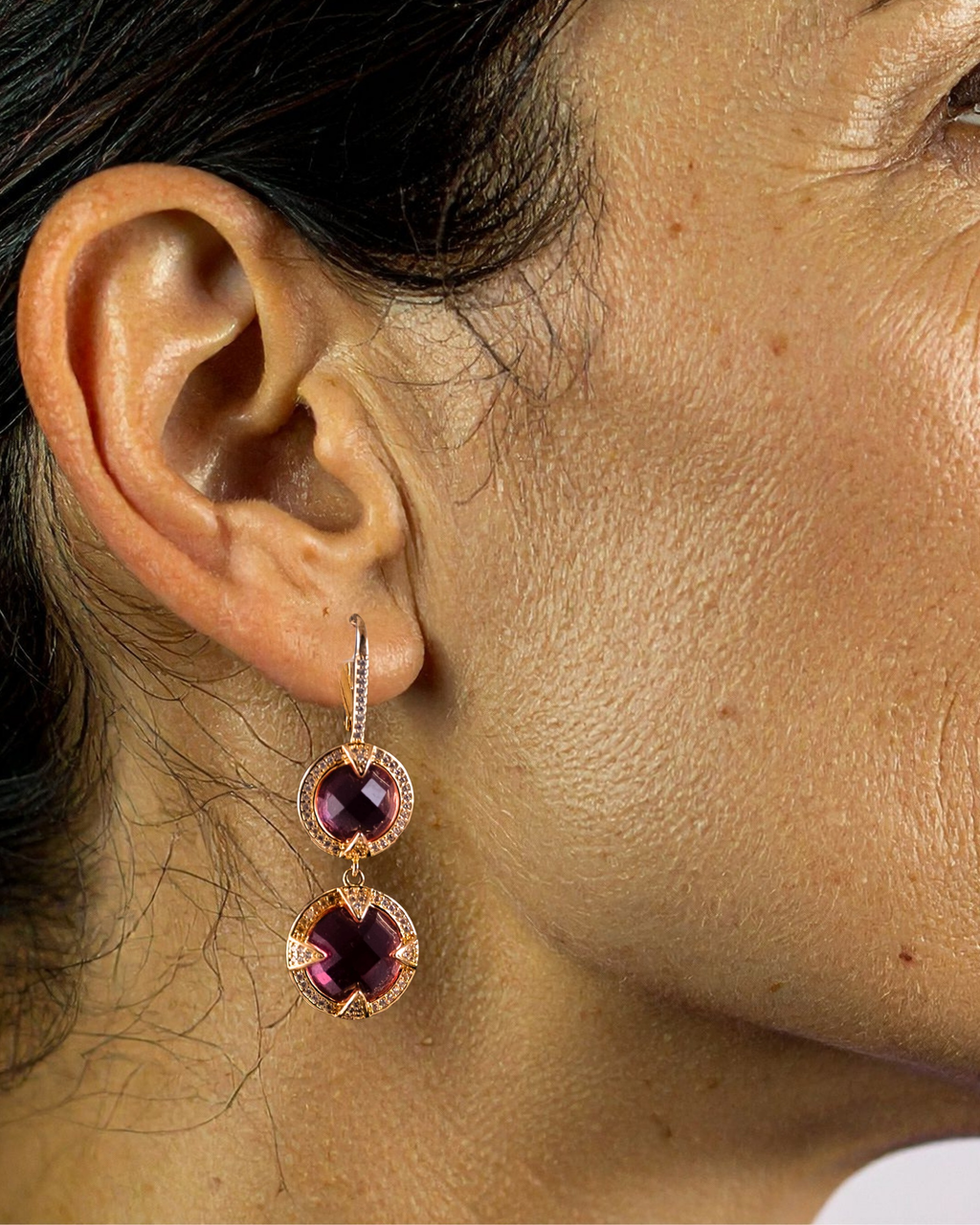 Close-up of a person wearing a pair of earrings with pink gemstones.