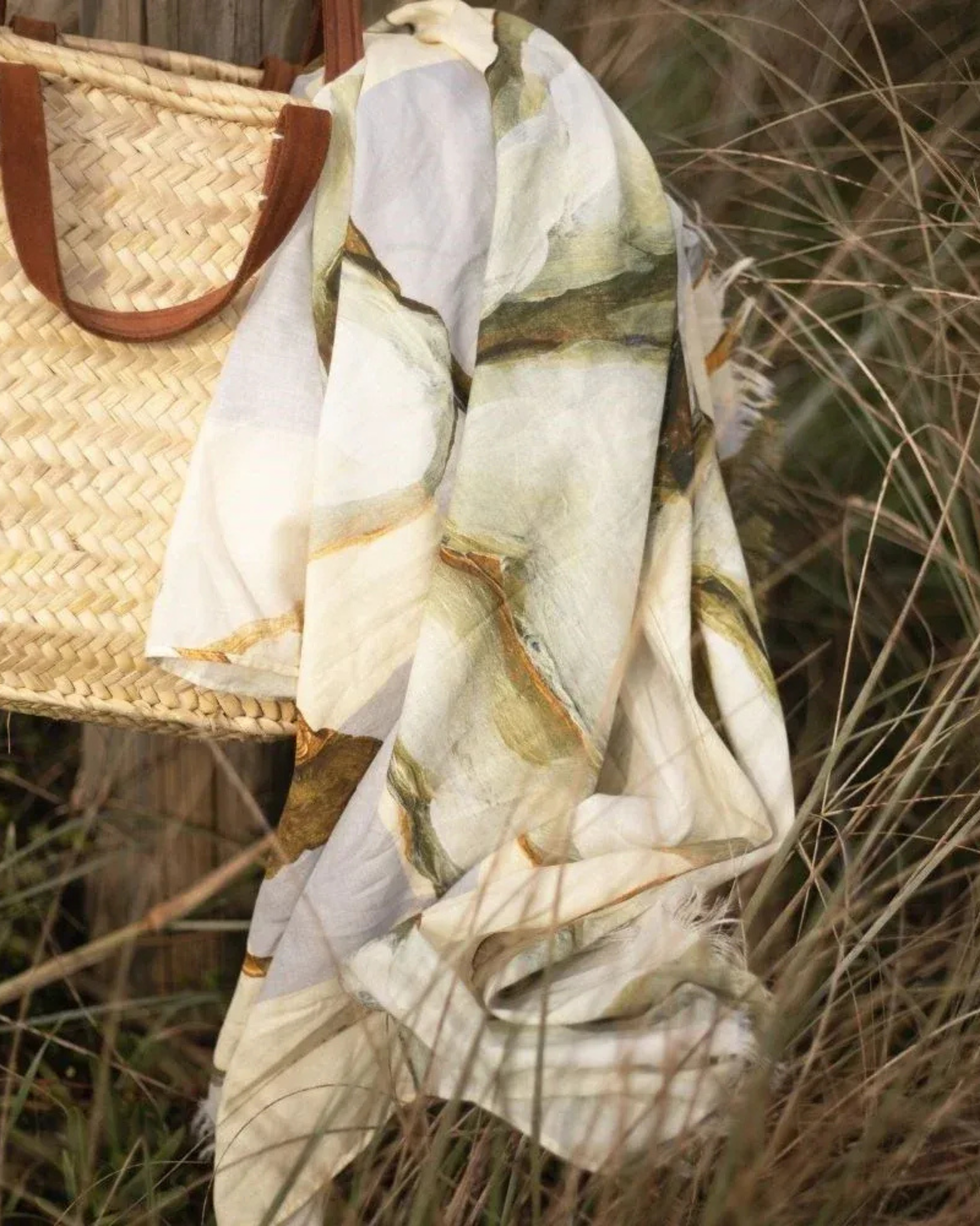 sarong with nature-themed design draped over a woven bag in a grassy setting