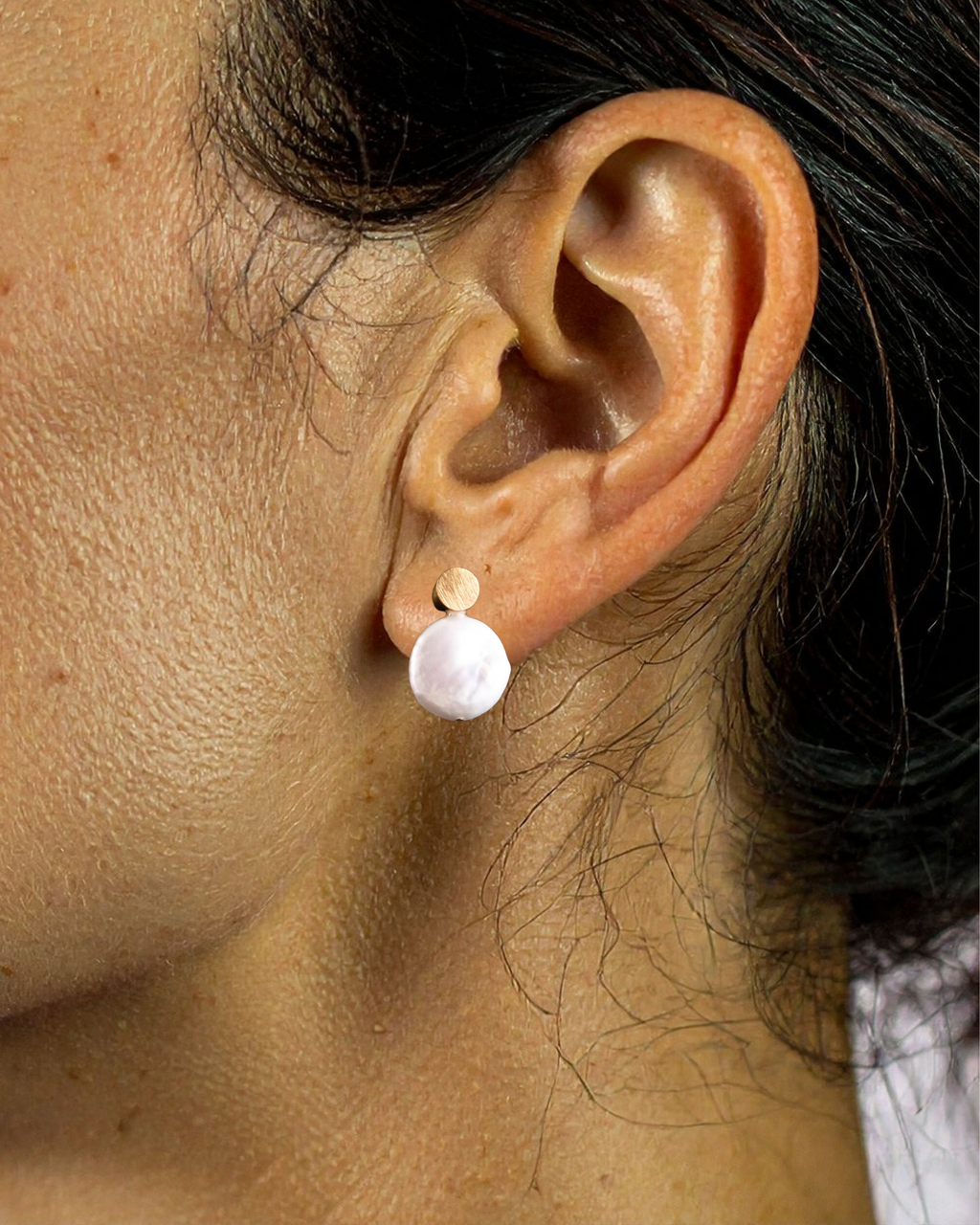 Close-up of an ear wearing a gold and white pearl earring.