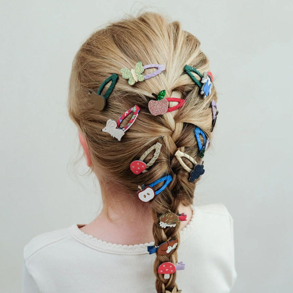 Person with braided hair adorned with various colorful hair clips on a plain background