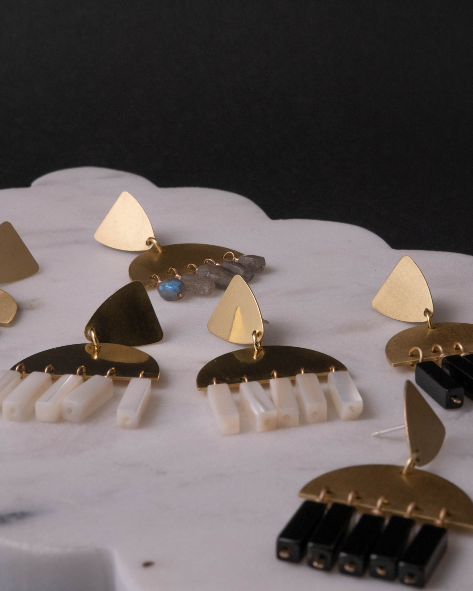 Set of gold and black earrings on a white display stand with a dark background