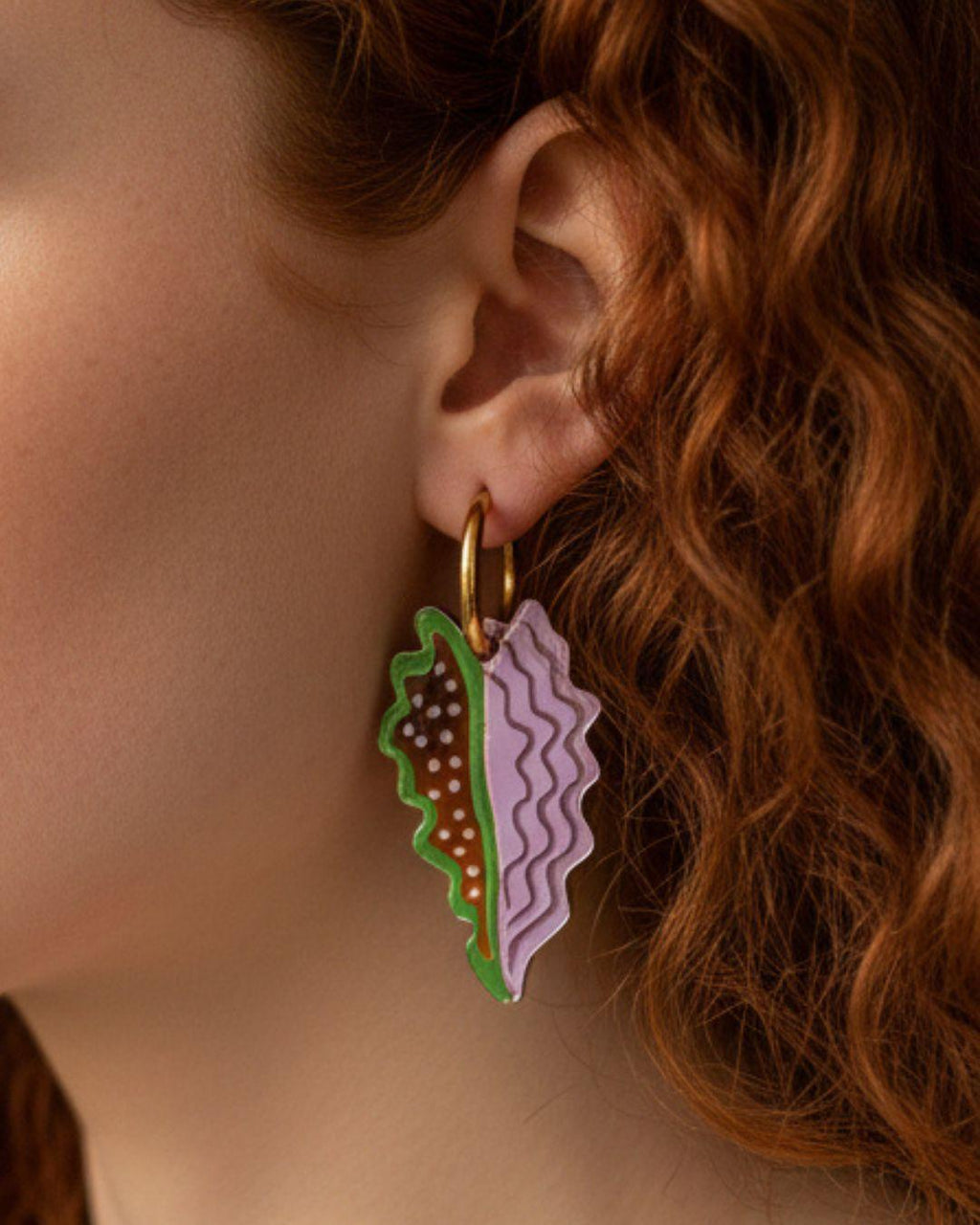 Close-up of a person wearing a unique leaf earring with a colourful design.