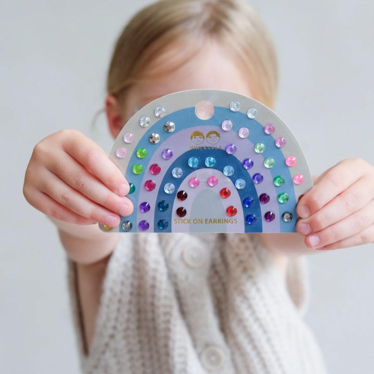 Child holding a card with rainbow-colored gemstones against a plain background