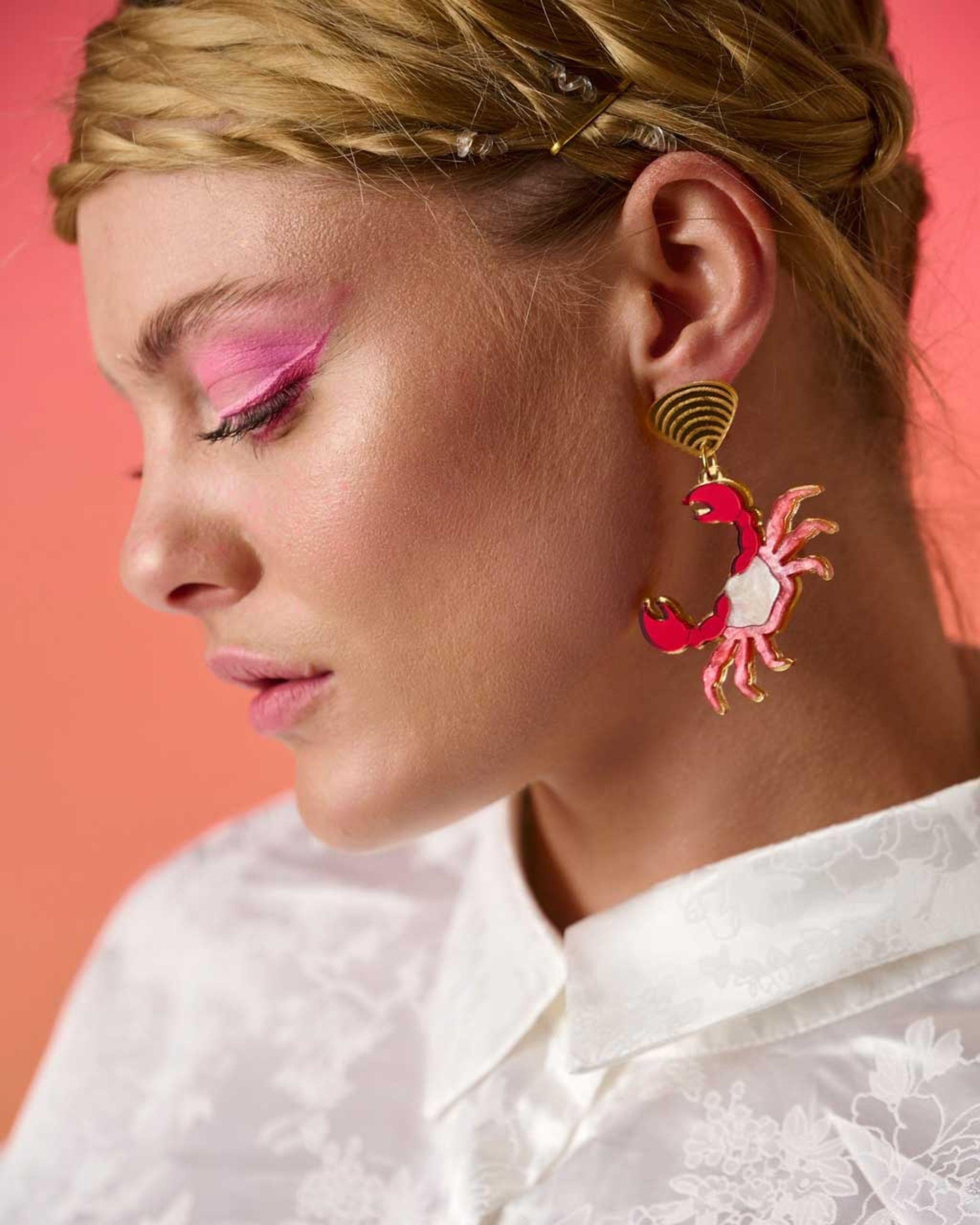 Person wearing a unique pink crab-shaped earring against a coral background