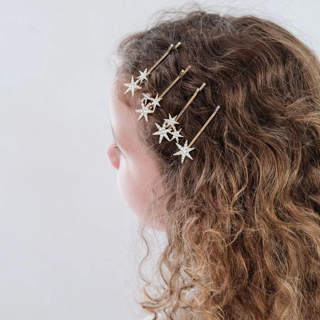 Person wearing gold hairpins with star designs in curly hair on a white background