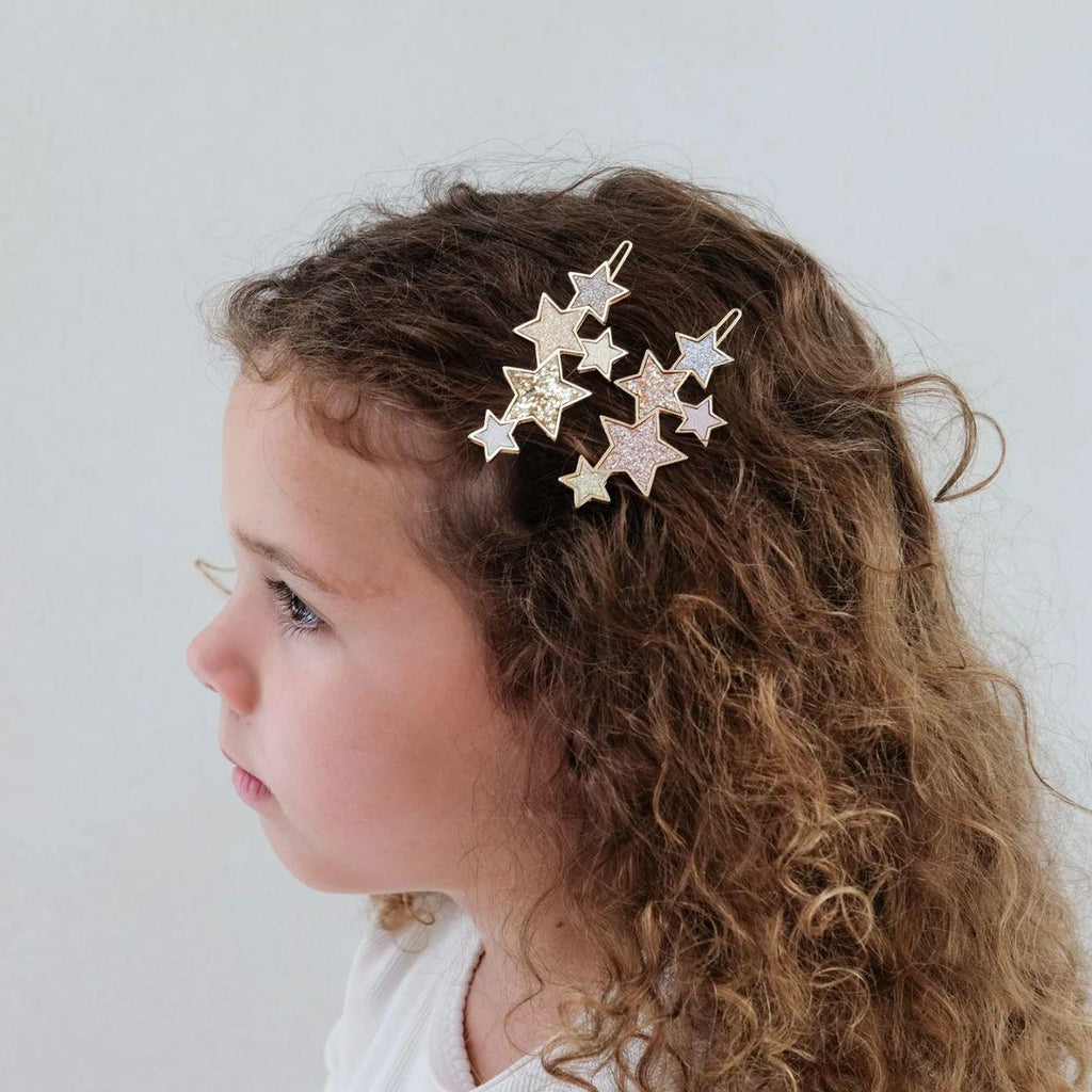 Child with curly hair wearing a star-shaped hair accessory against a plain background