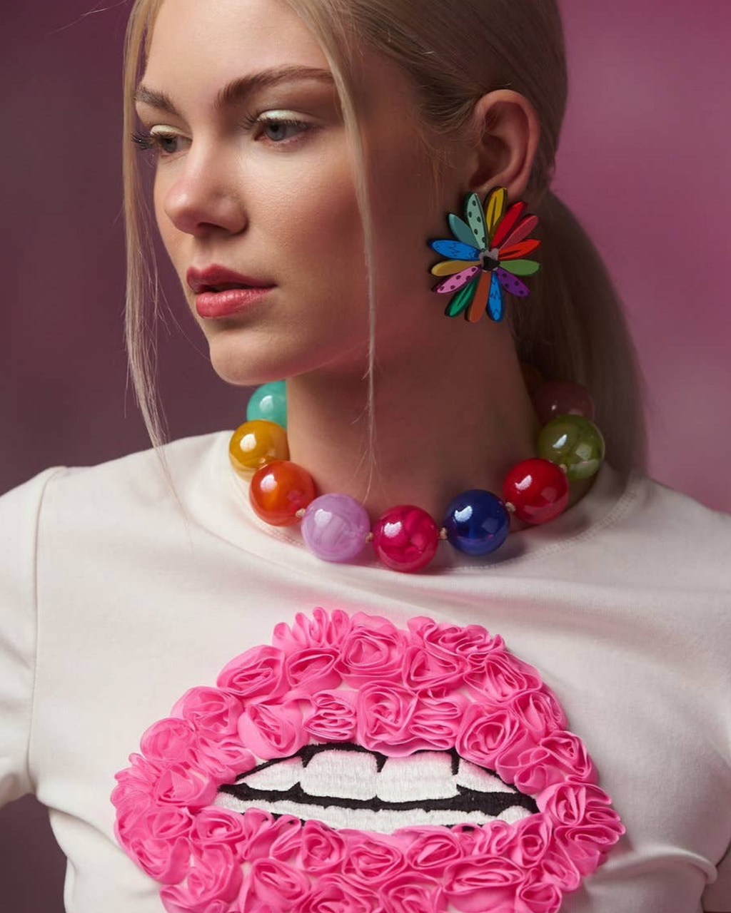 Person wearing colourful jewellery with a pink and white lip design on a white shirt.