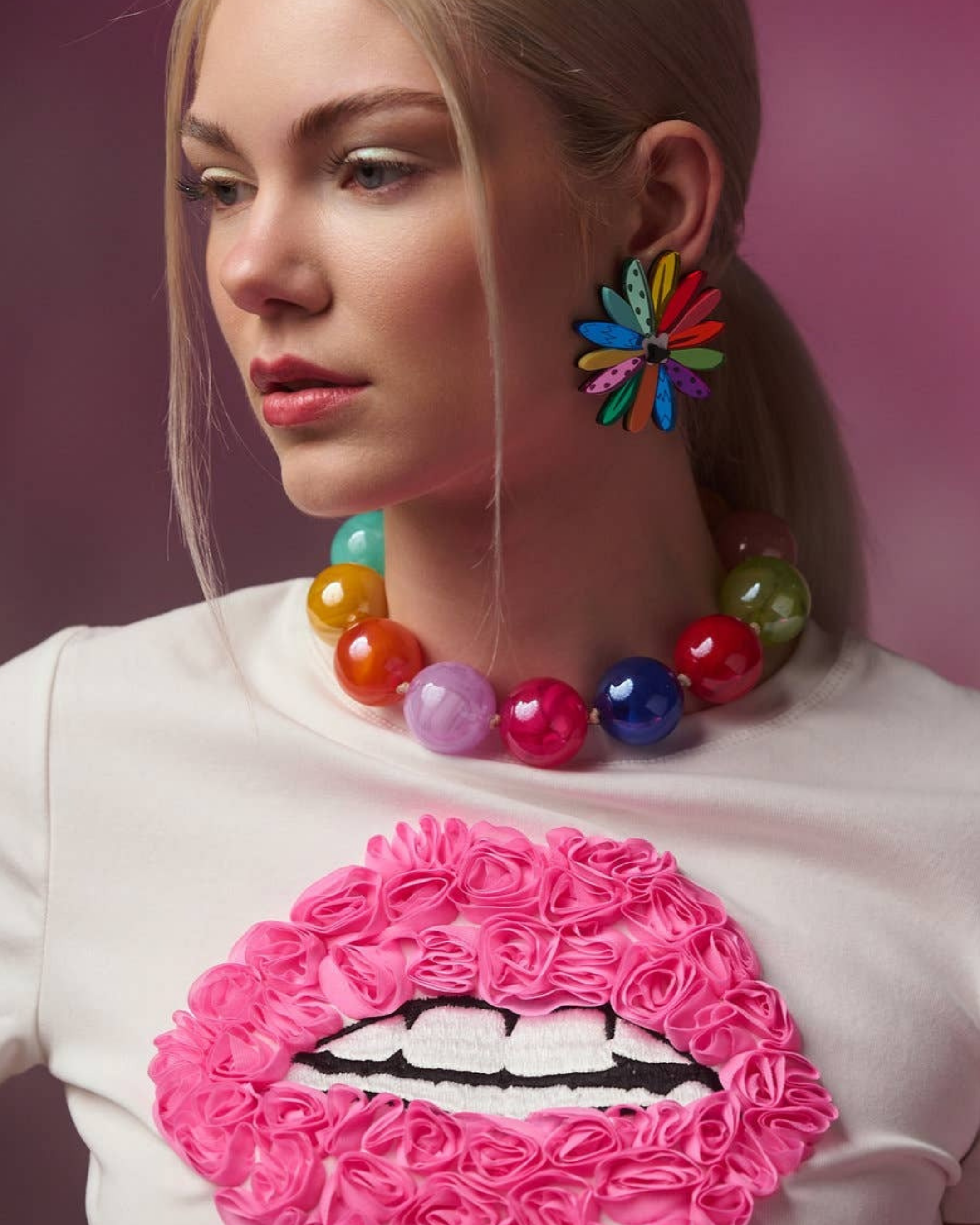 Person wearing colourful jewellery with a pink and white lip design on a white shirt.