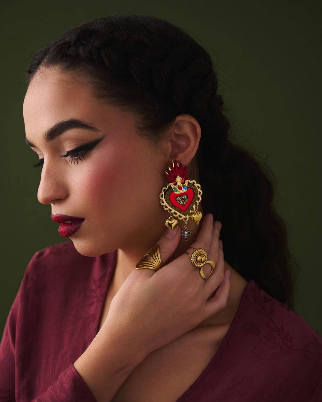 Person wearing ornate heart earrings and a ring against a dark background